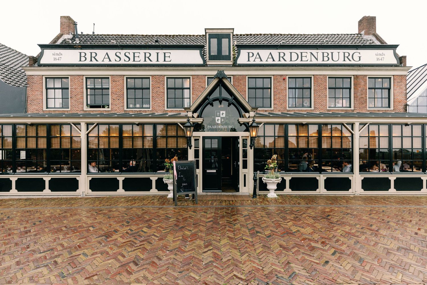 A panoramic view of a historic Dutch brasserie building with large windows and traditional brick architecture.