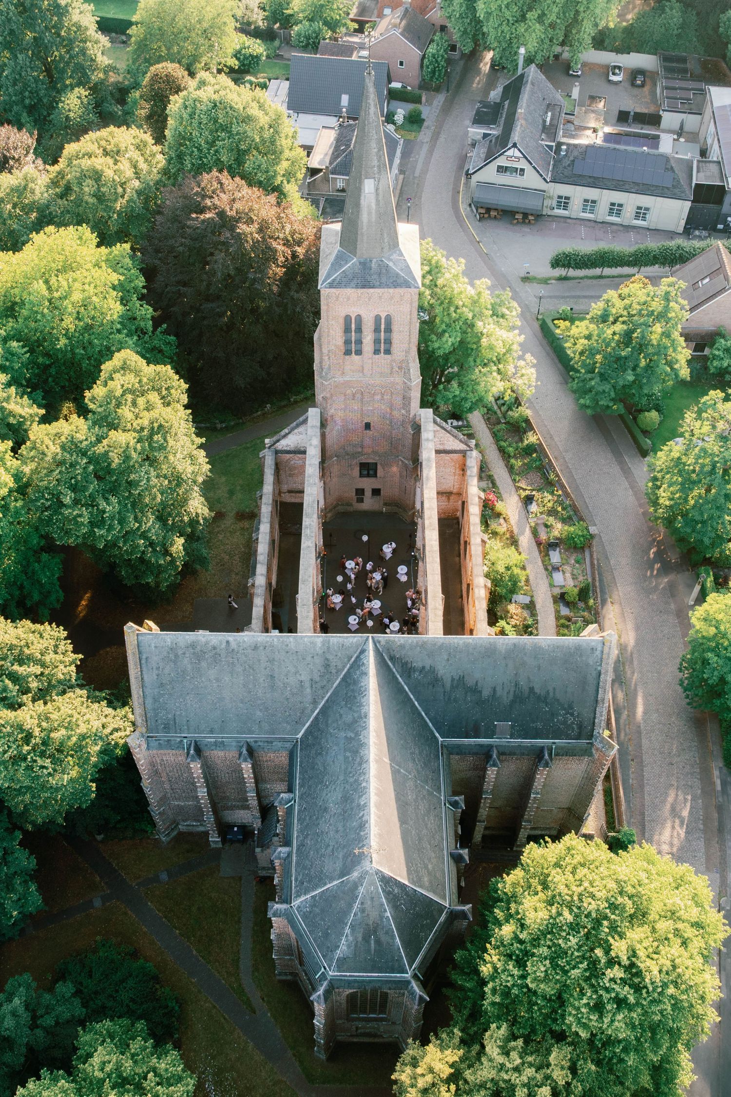 Aerial view of a traditional church with gray roof and tall spire surrounded by lush green trees in a residential area.