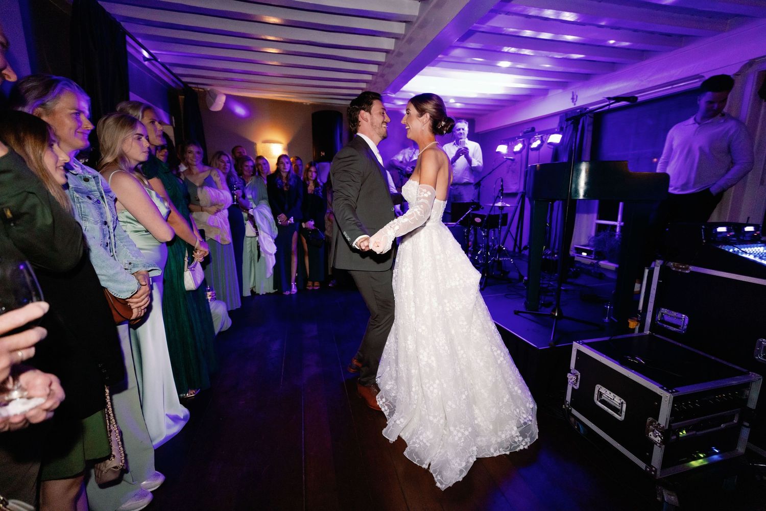 Wedding reception dance floor illuminated with purple lighting as guests celebrate and dance together.