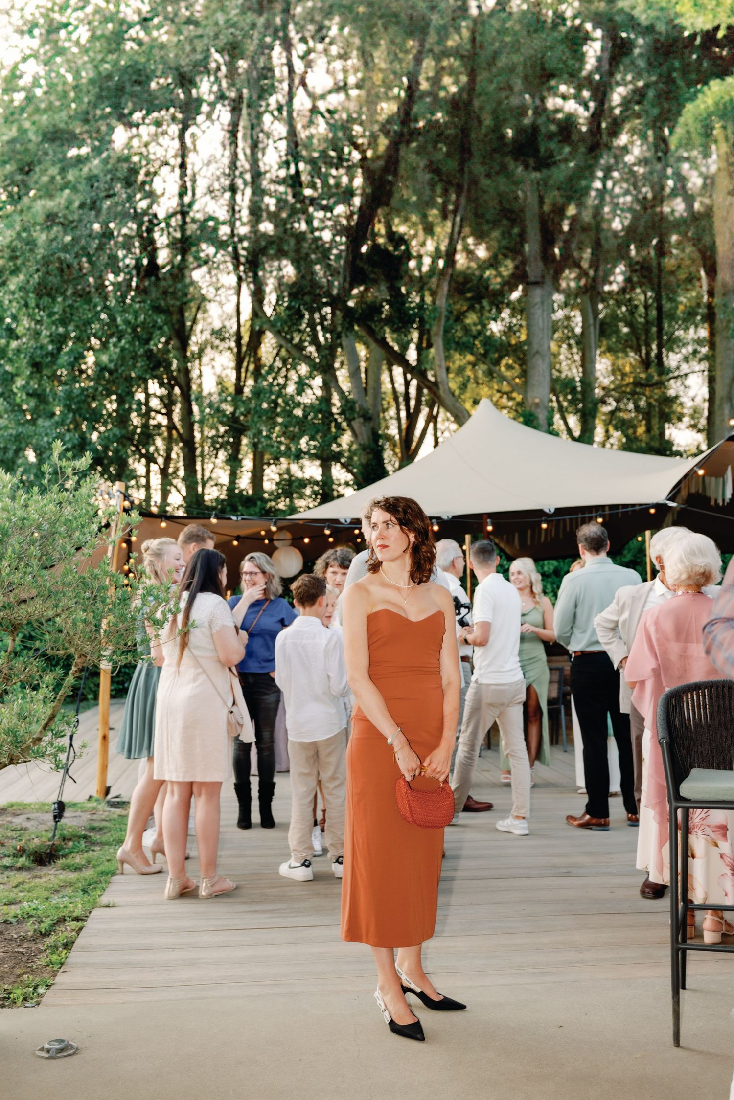 Guests mingle and socialize at an outdoor garden reception under a white canopy surrounded by lush greenery.