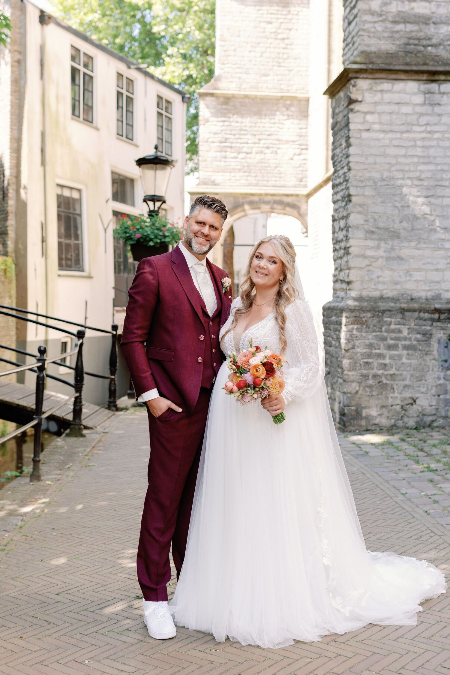 A wedding couple poses together against a stone wall backdrop in a romantic outdoor setting.