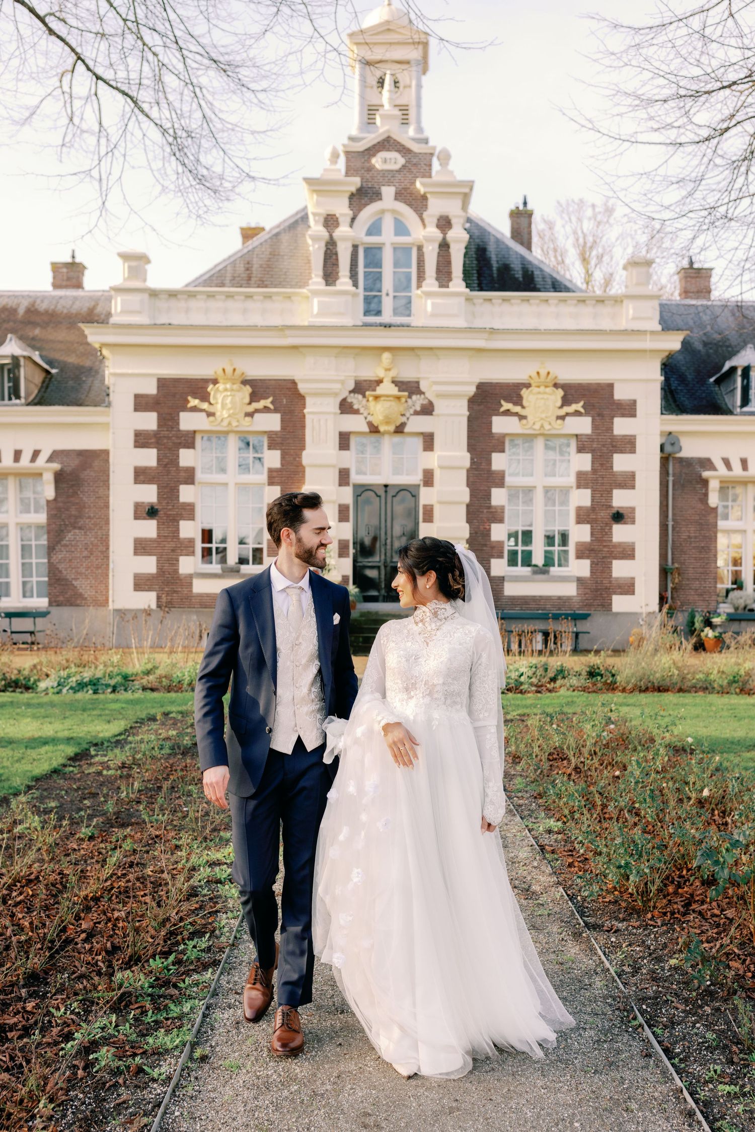 A bride and groom share romantic moments outside a historic brick building with elegant white architectural details.