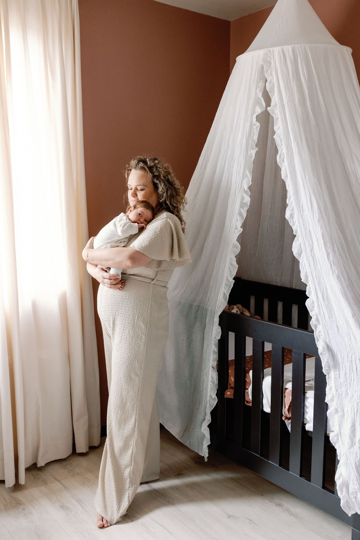 A tender moment between parent and baby near a white canopy crib.