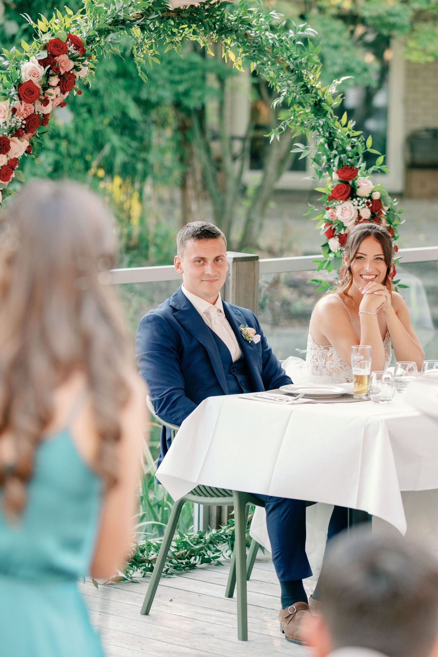 Outdoor wedding reception seating with floral arch and white tablecloths.