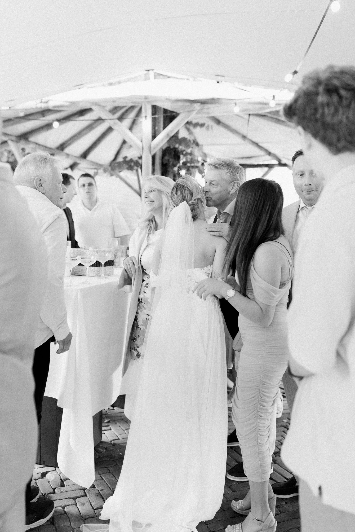 Wedding guests in all-white attire gathered under white umbrellas at an outdoor celebration.
