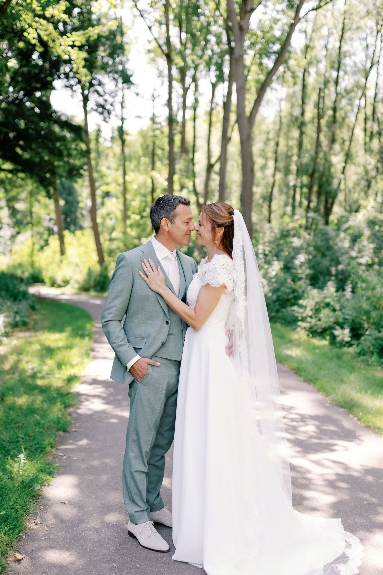 A couple shares intimate moments on a sunlit forest path during their wedding photoshoot.