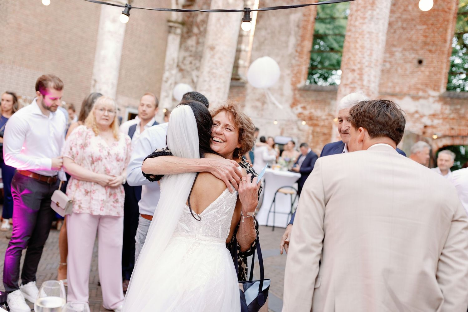 Wedding guests dance and celebrate on an outdoor patio decorated with string lights at a rustic venue.