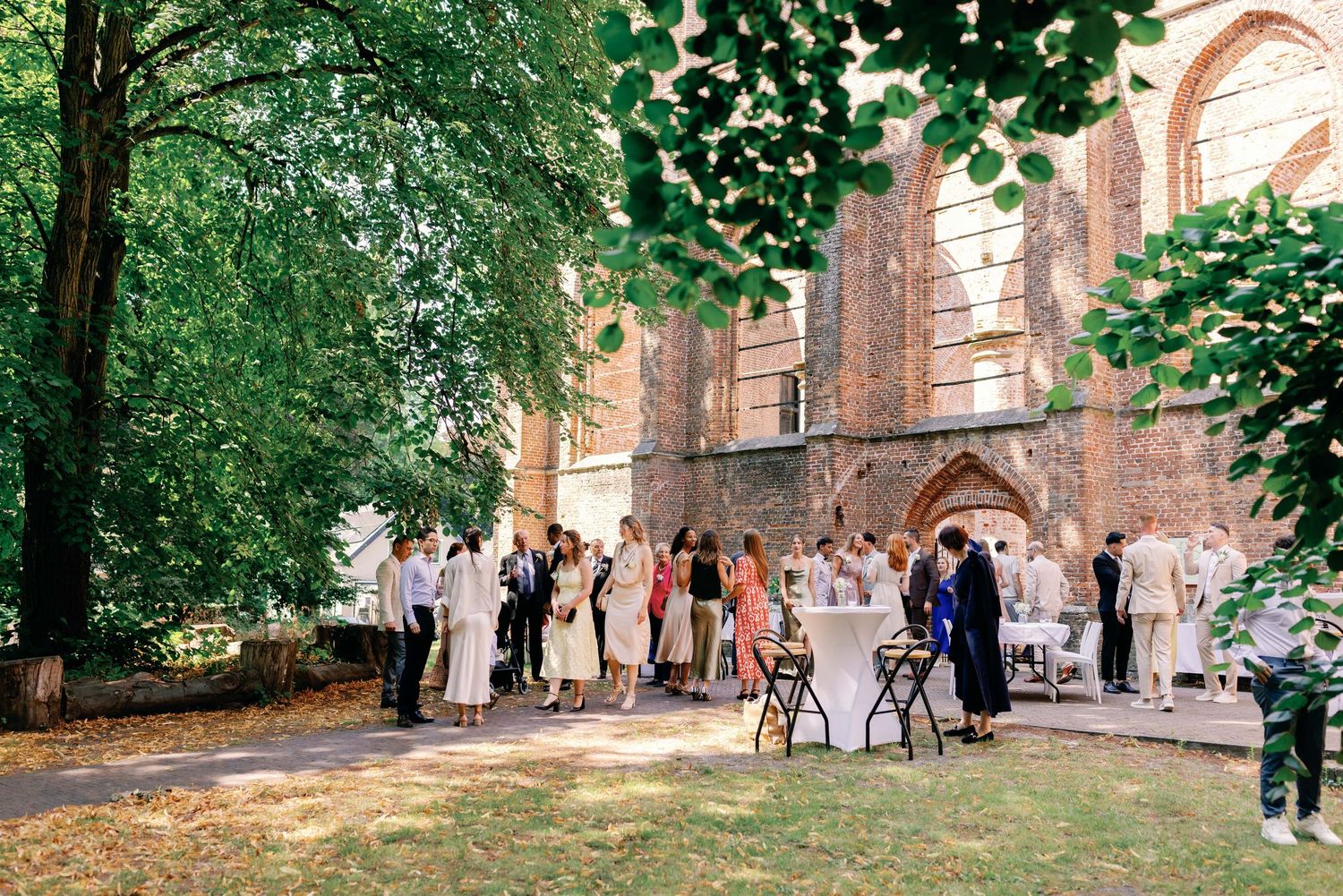 Wedding guests gather on a lush green lawn outside a historic brick church building during an outdoor celebration.