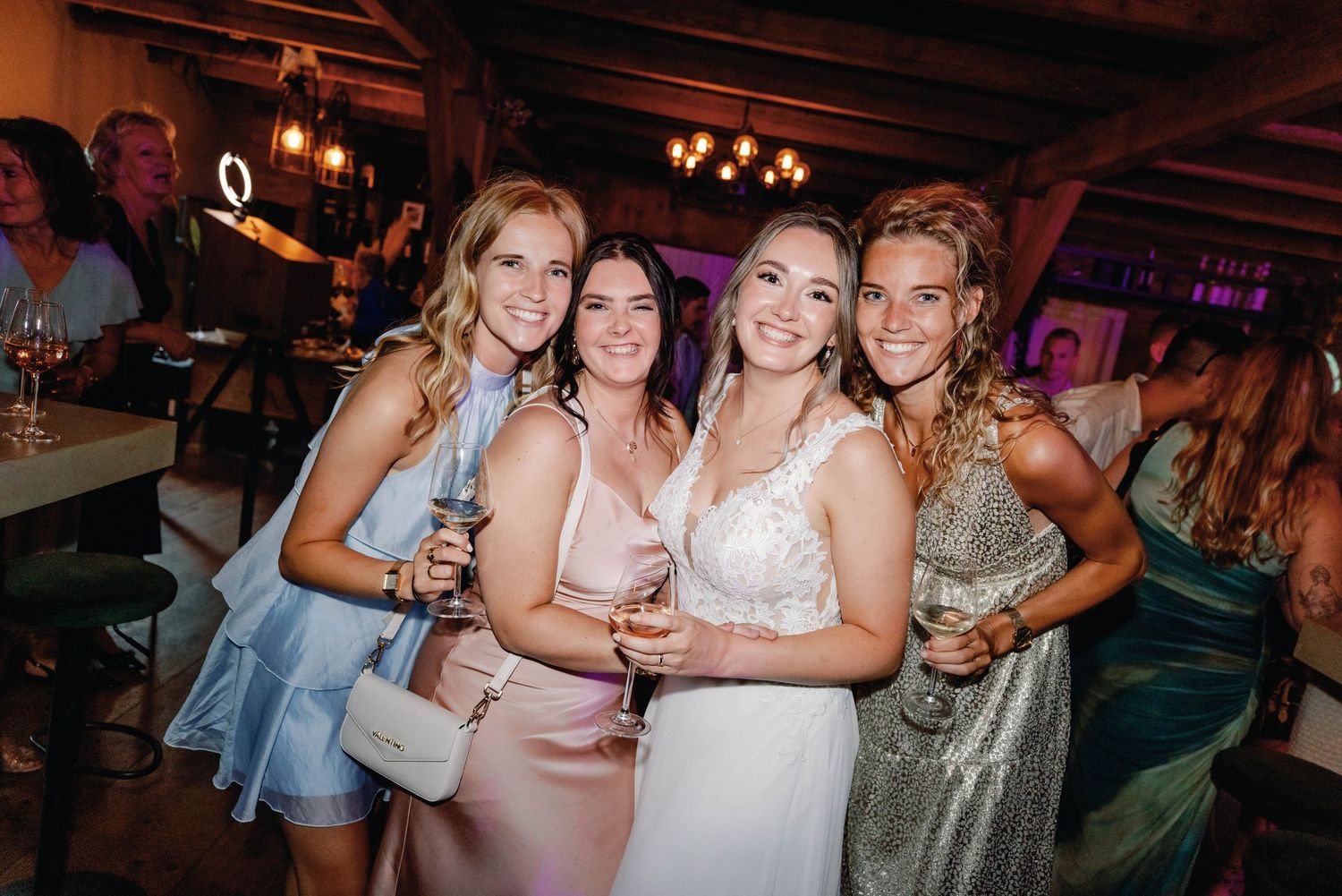 A group of people dancing and celebrating at a wedding reception in a rustic venue with warm lighting.