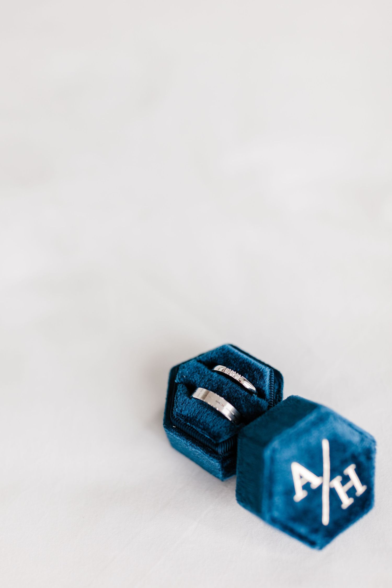 A blue velvet ring box with monogram holds wedding bands against a white background.