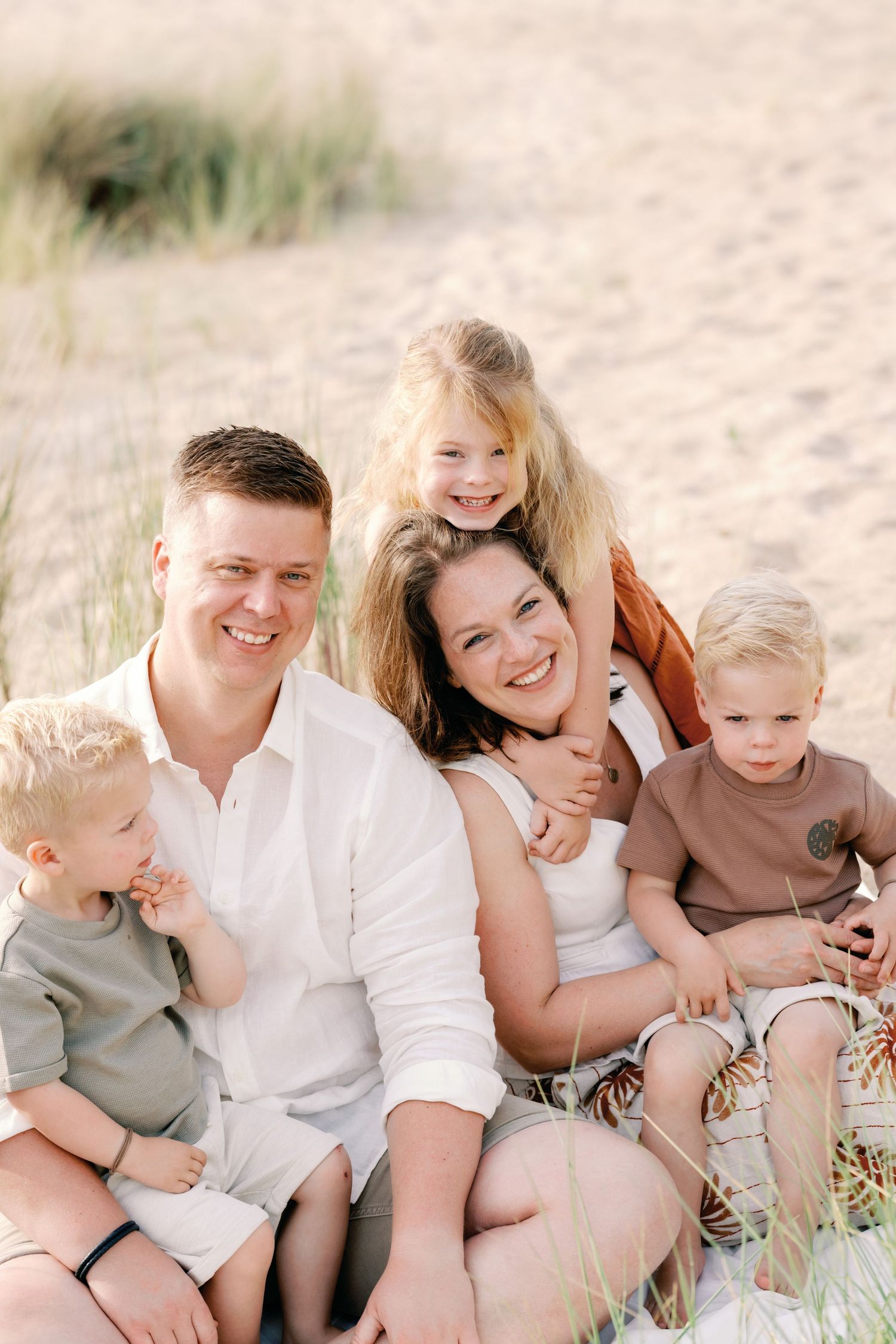 Happy family of five smiling together on a sandy beach, parents with three young children enjoying a sunny day.