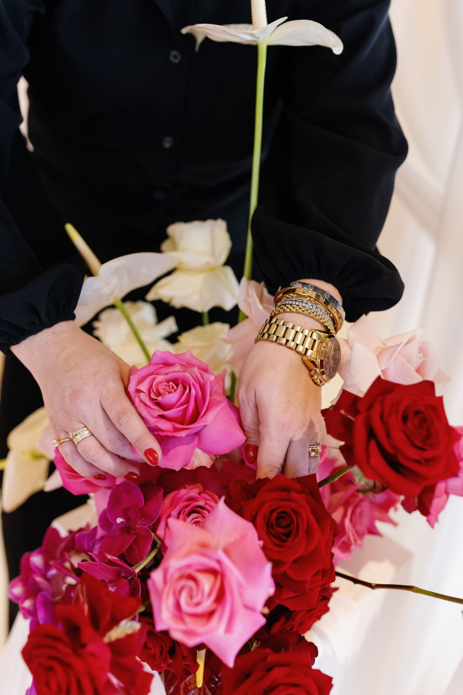 A row of pink and red roses with hands wearing gold rings holding bouquets against a dark background.