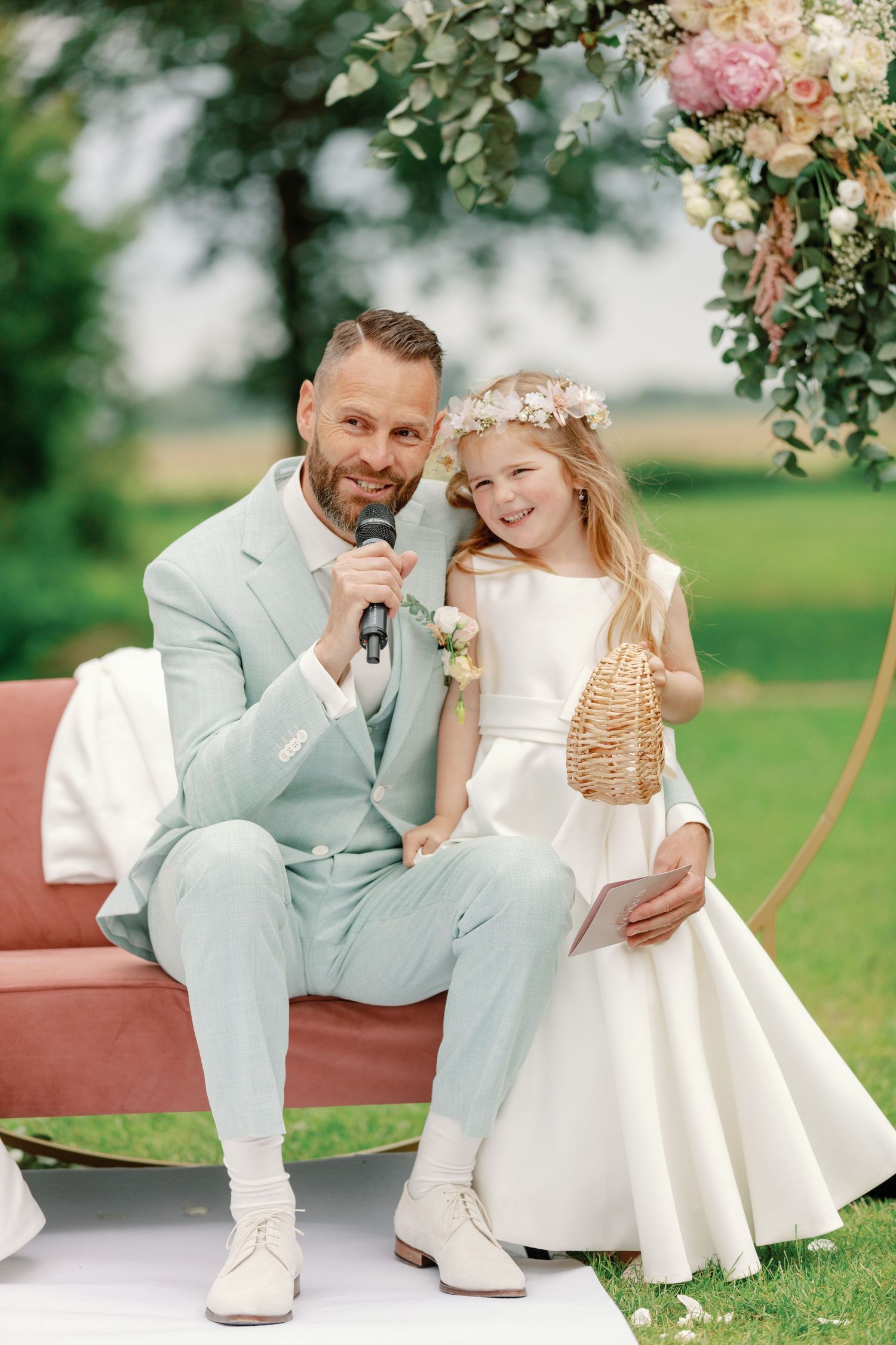 A sweet outdoor wedding moment captured on a red bench under floral decorations in a garden setting.