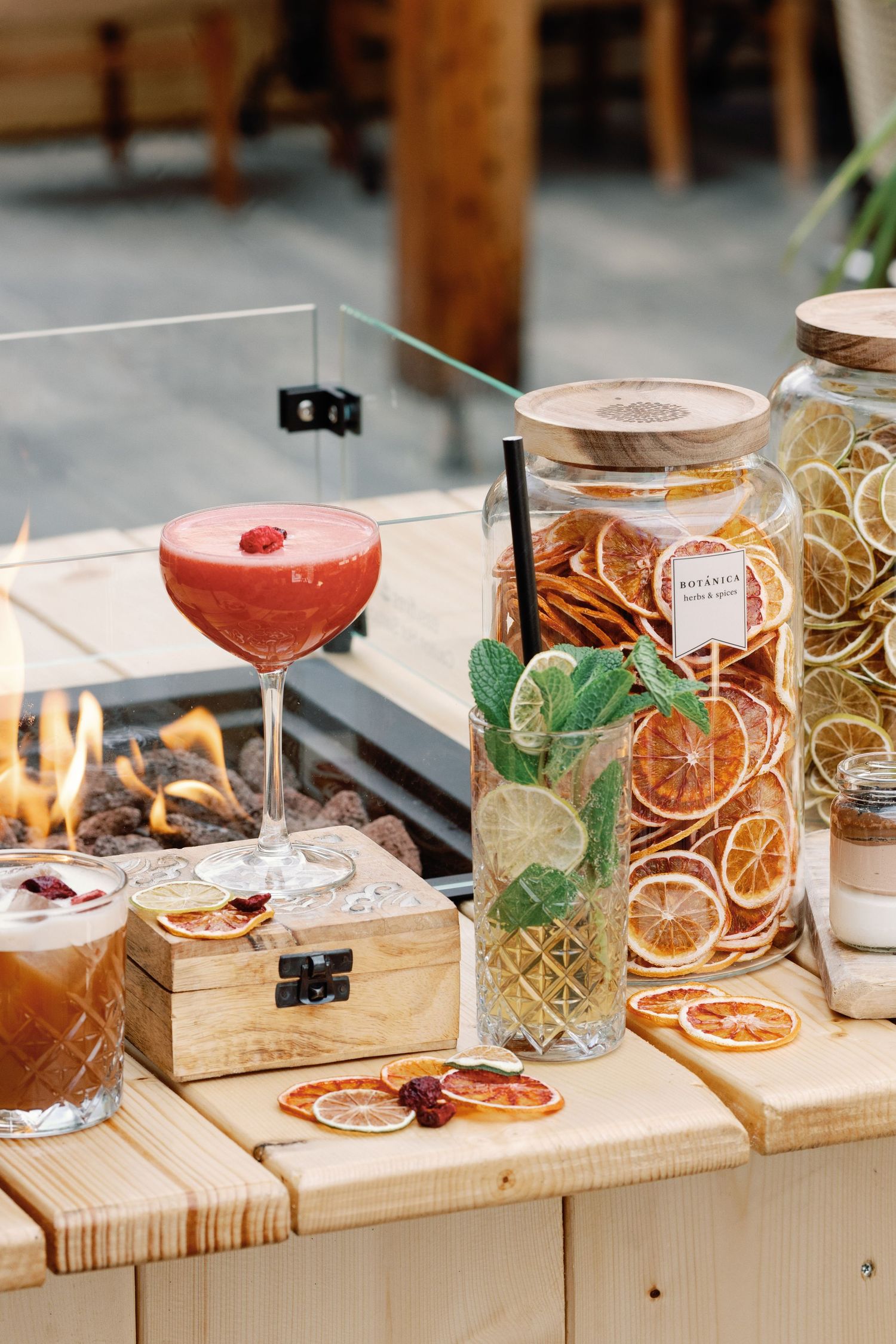Artisanal cocktails garnished with dried citrus and herbs displayed on wooden serving boards in a modern bar setting.