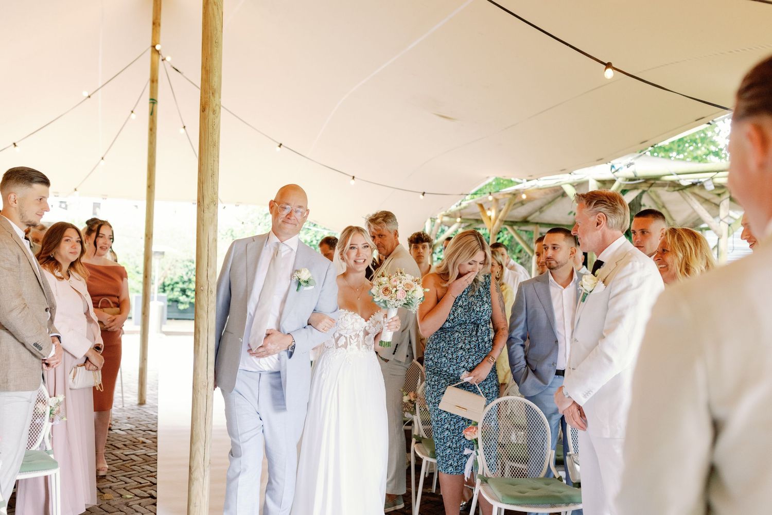Wedding party in light gray suits and dresses dance together in a reception venue with white tent canopy.