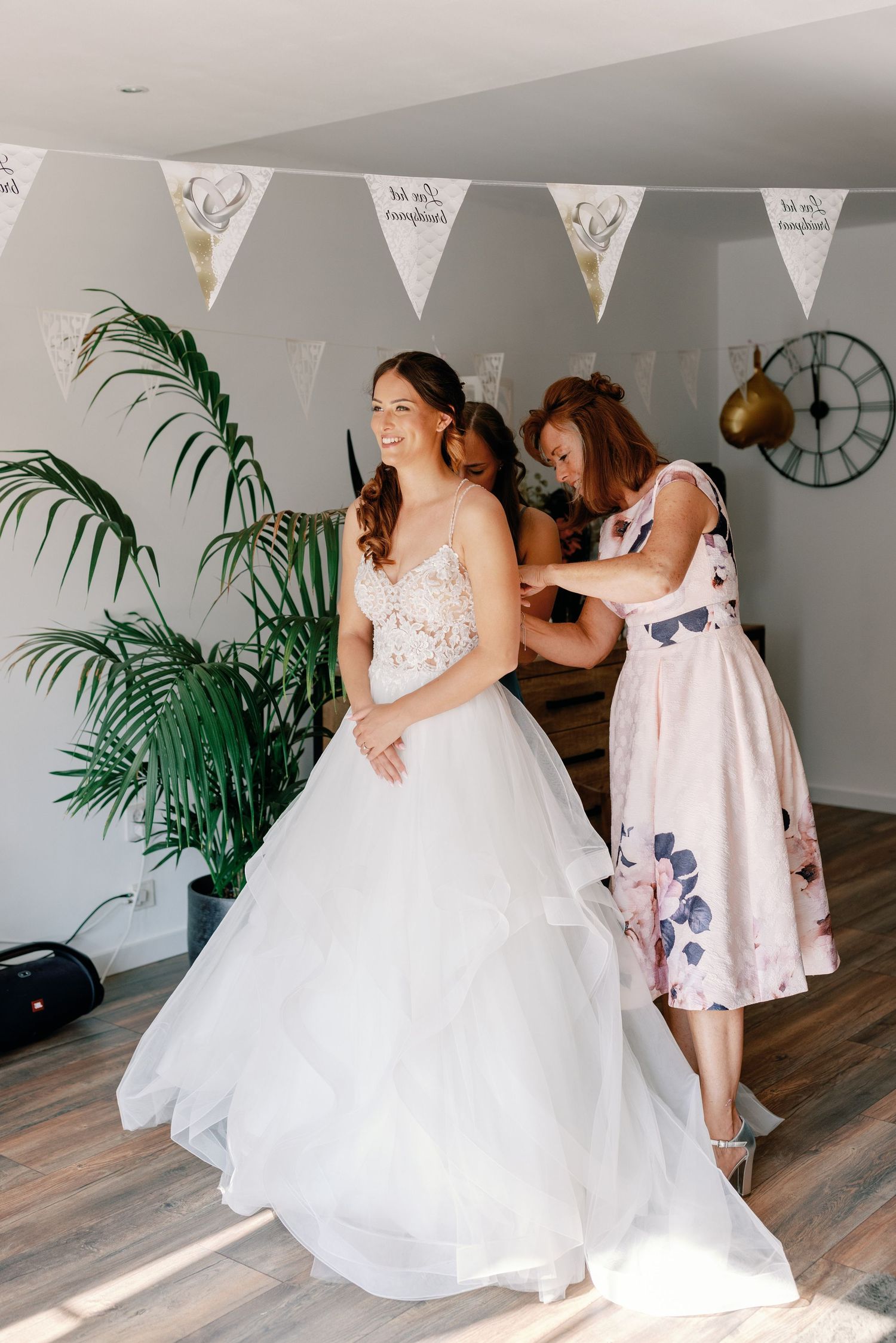 A wedding dress being adjusted in a room decorated with white bunting and tropical plants.