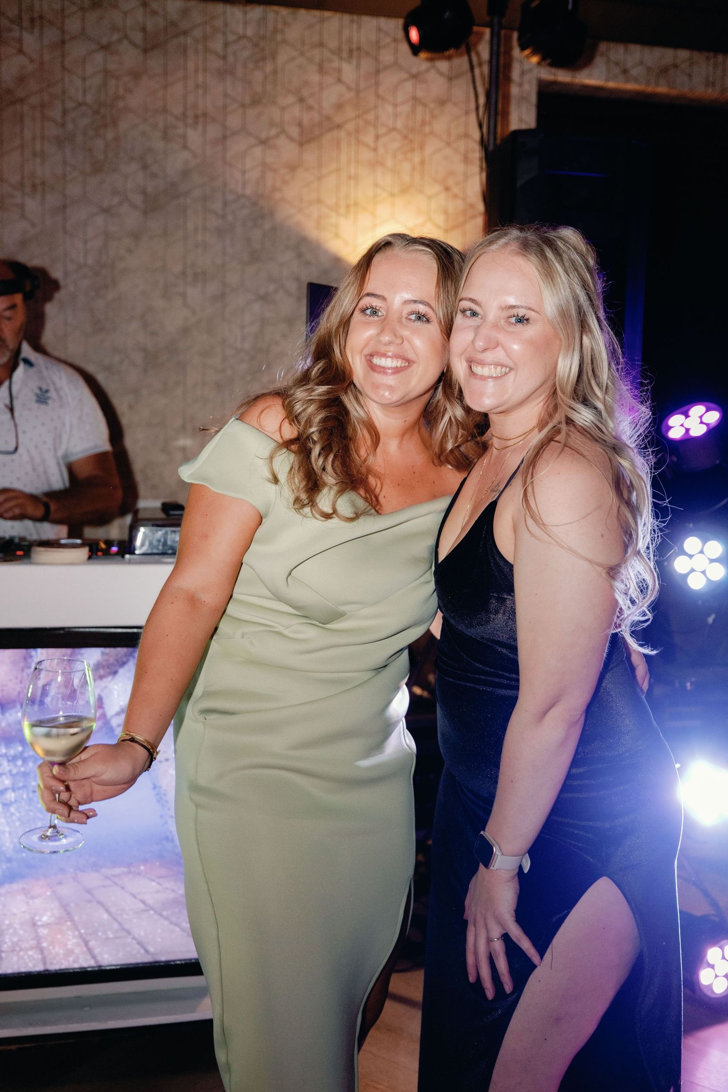 Two wedding guests in elegant dresses pose together on the dance floor.
