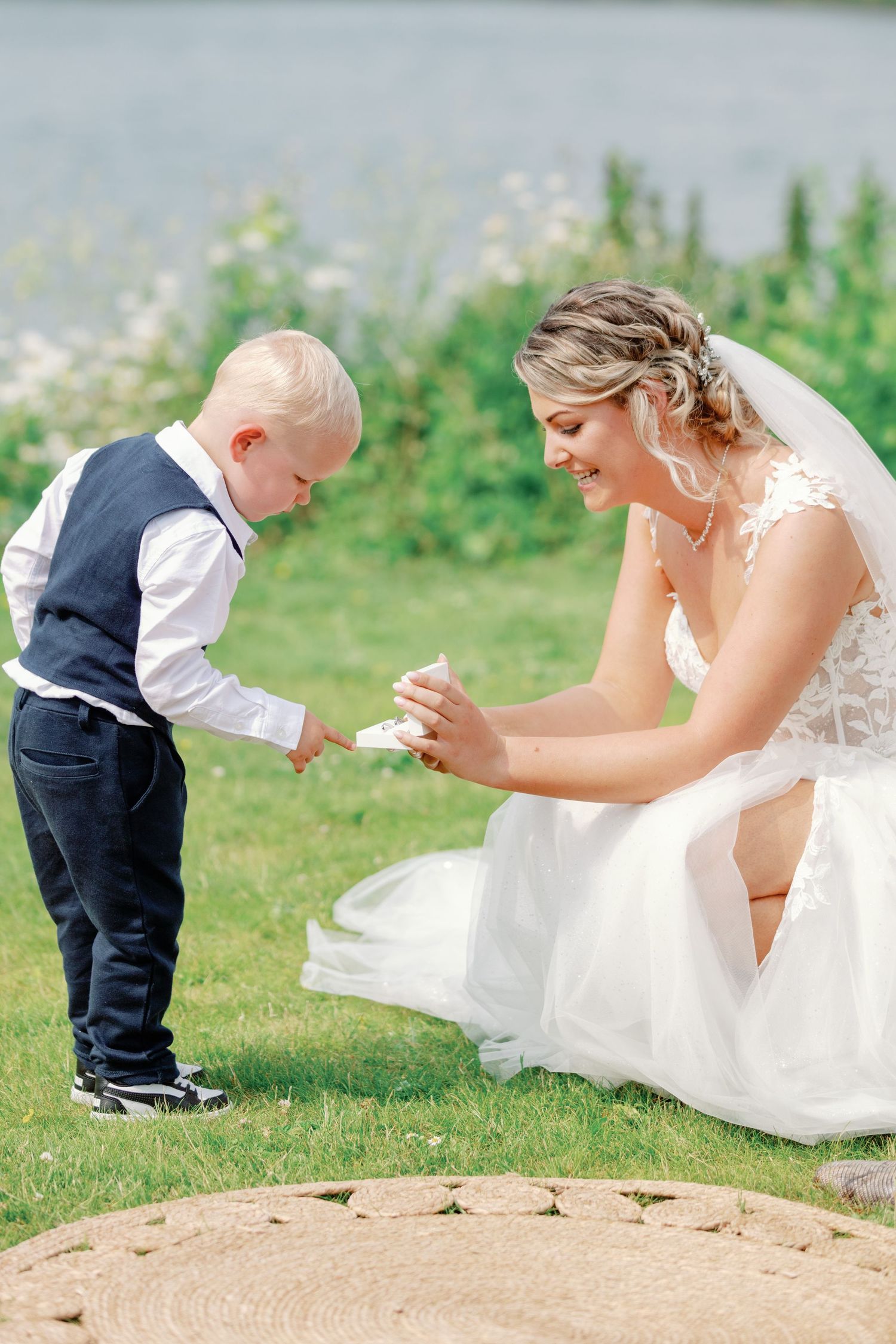 Sweet moment of a bride in white dress playing with a small child on grassy ground.