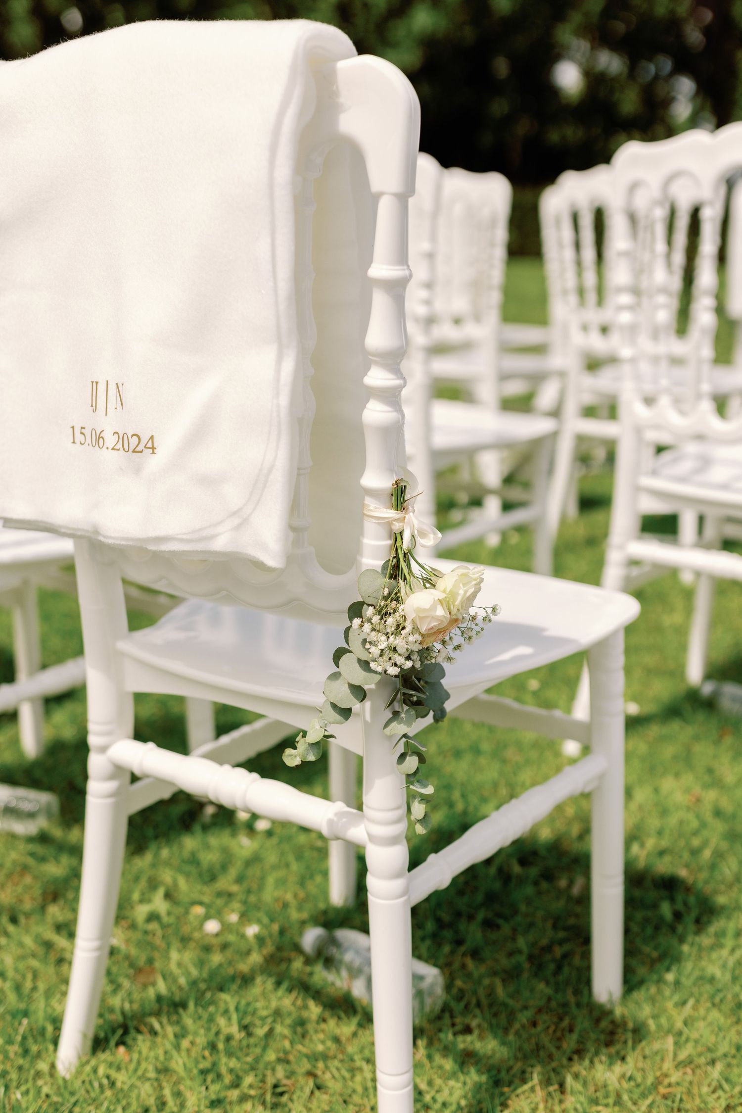 White wooden chairs arranged outdoors on grass for a garden wedding ceremony with delicate floral decorations.
