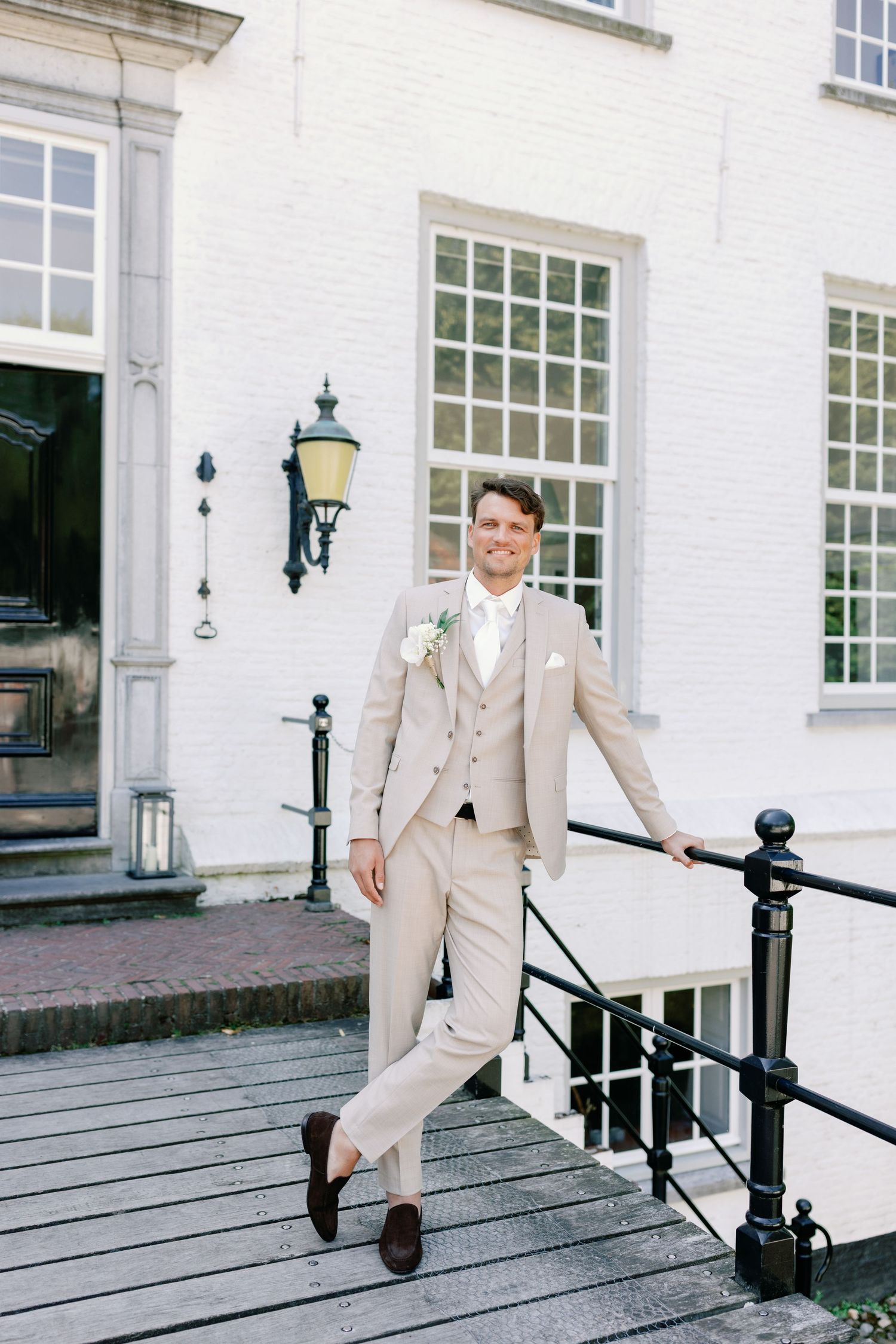 A person in a beige suit poses on the steps of a white building with classic Georgian-style windows and lantern.