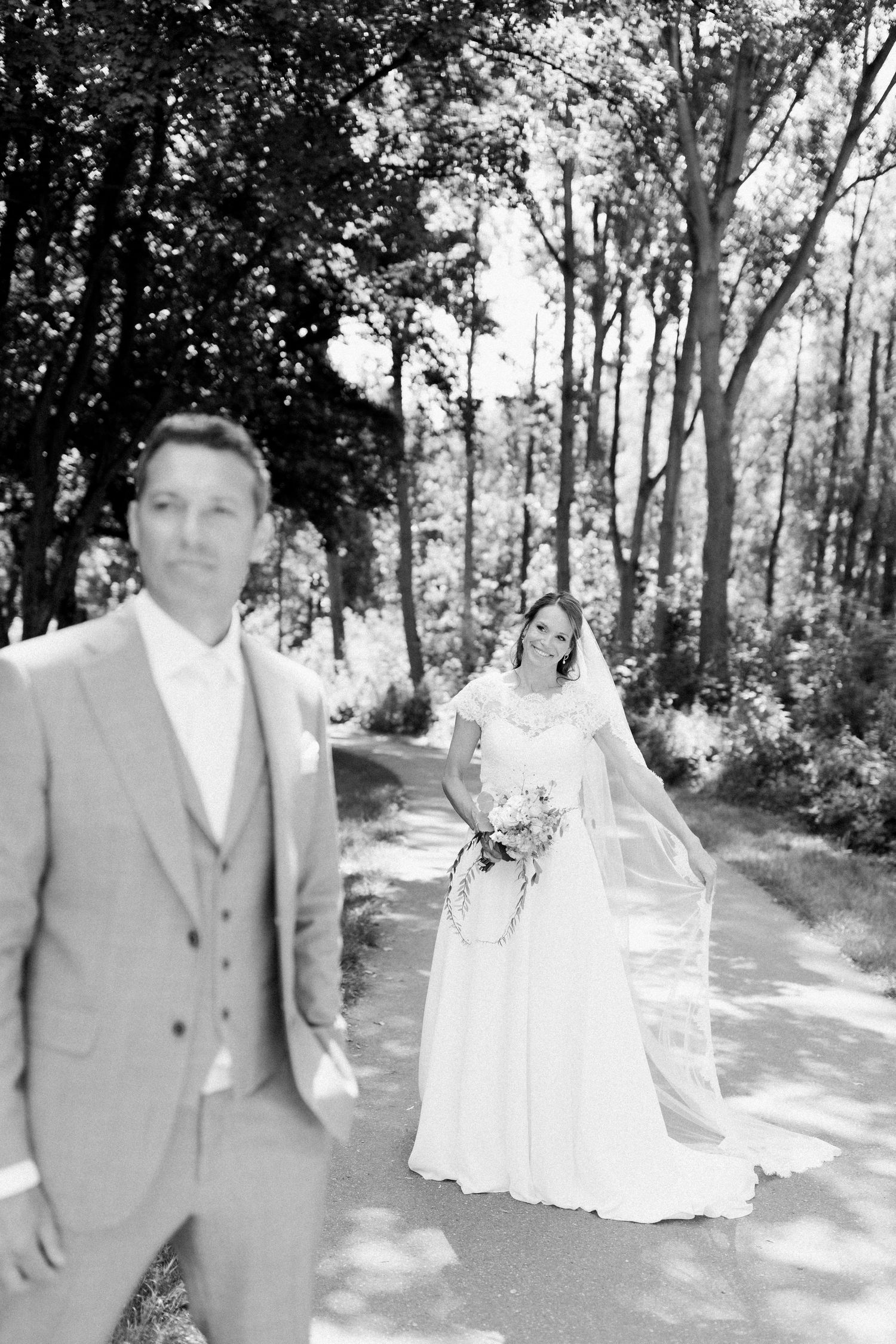 A wedding couple stands together on a wooded path during their outdoor photo session.
