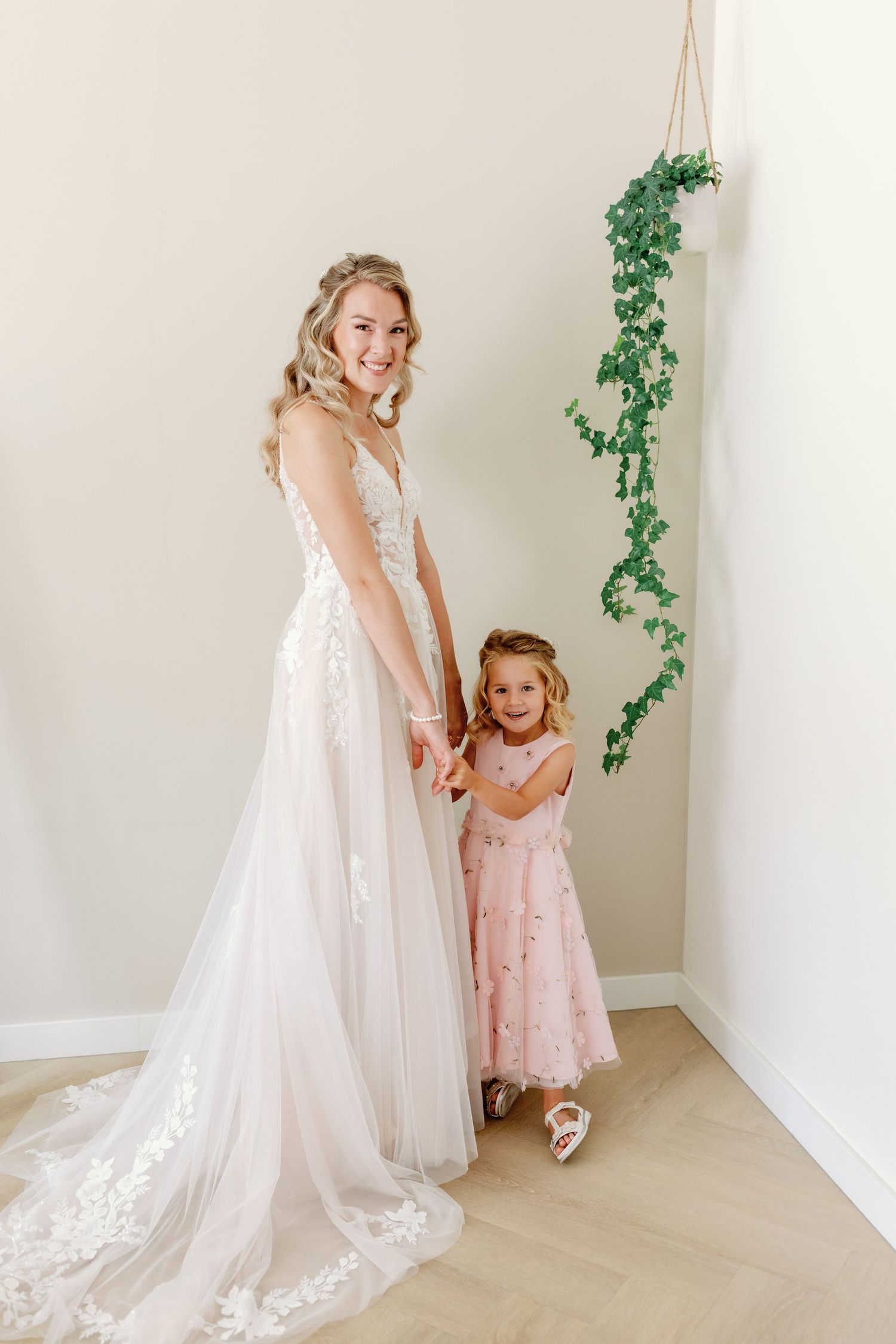A wedding dress and pink dress are worn in a bright white studio space with delicate ivy decorations.