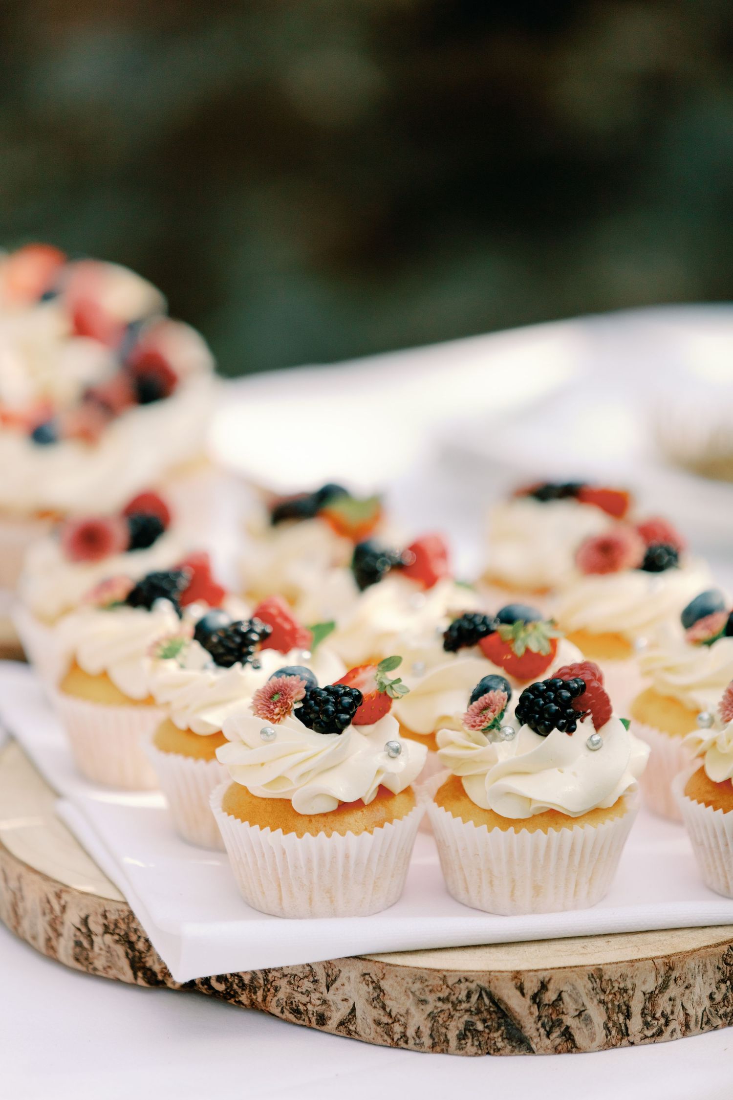 Mini cupcakes decorated with berries and whipped cream displayed on rustic wood slices.