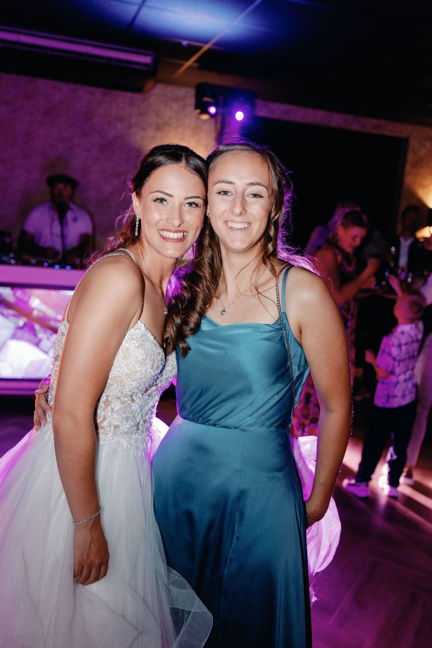 Two guests pose together at a wedding reception under purple lighting.