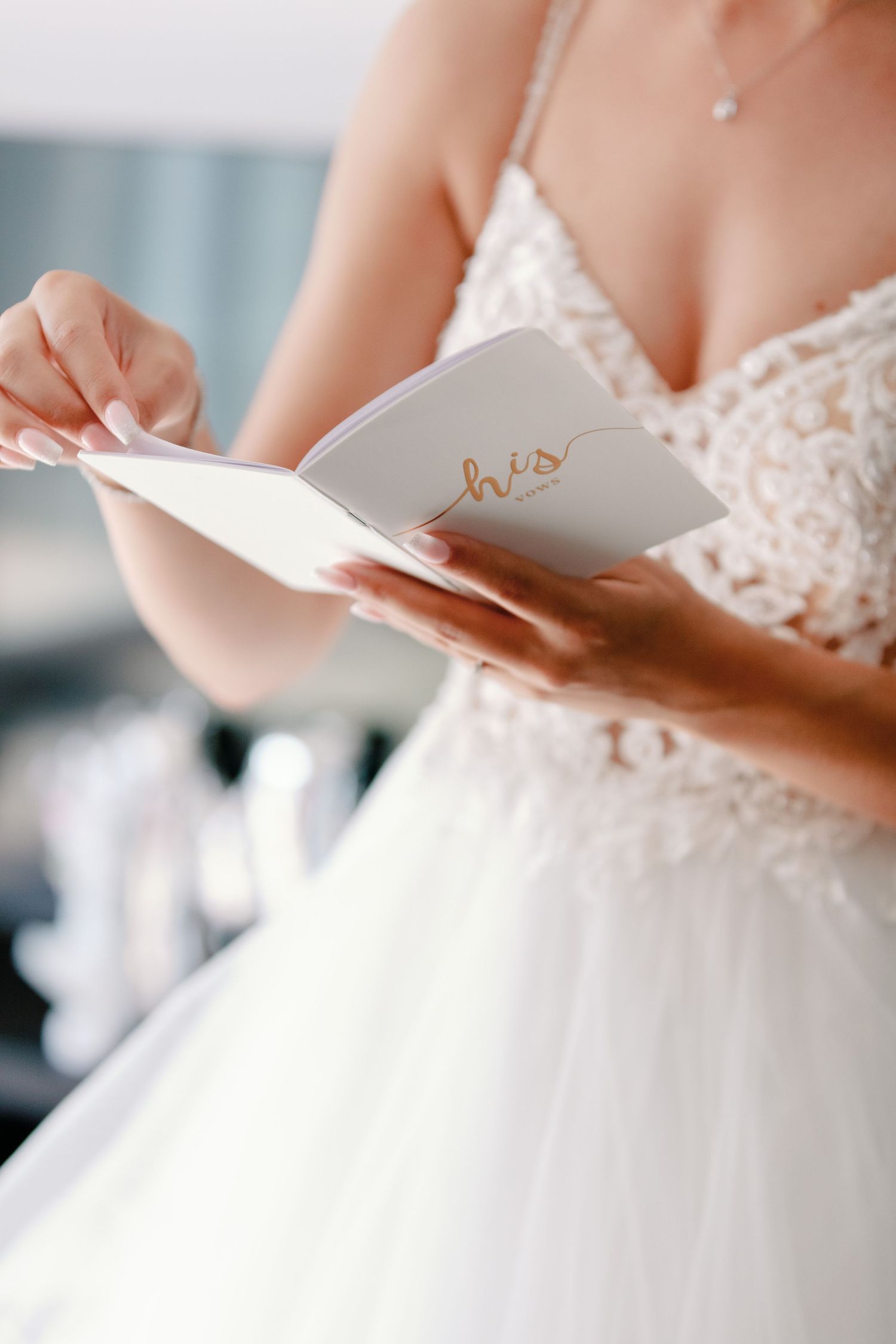 Detail shot of hands holding a small white book while wearing an elegant lace wedding gown.