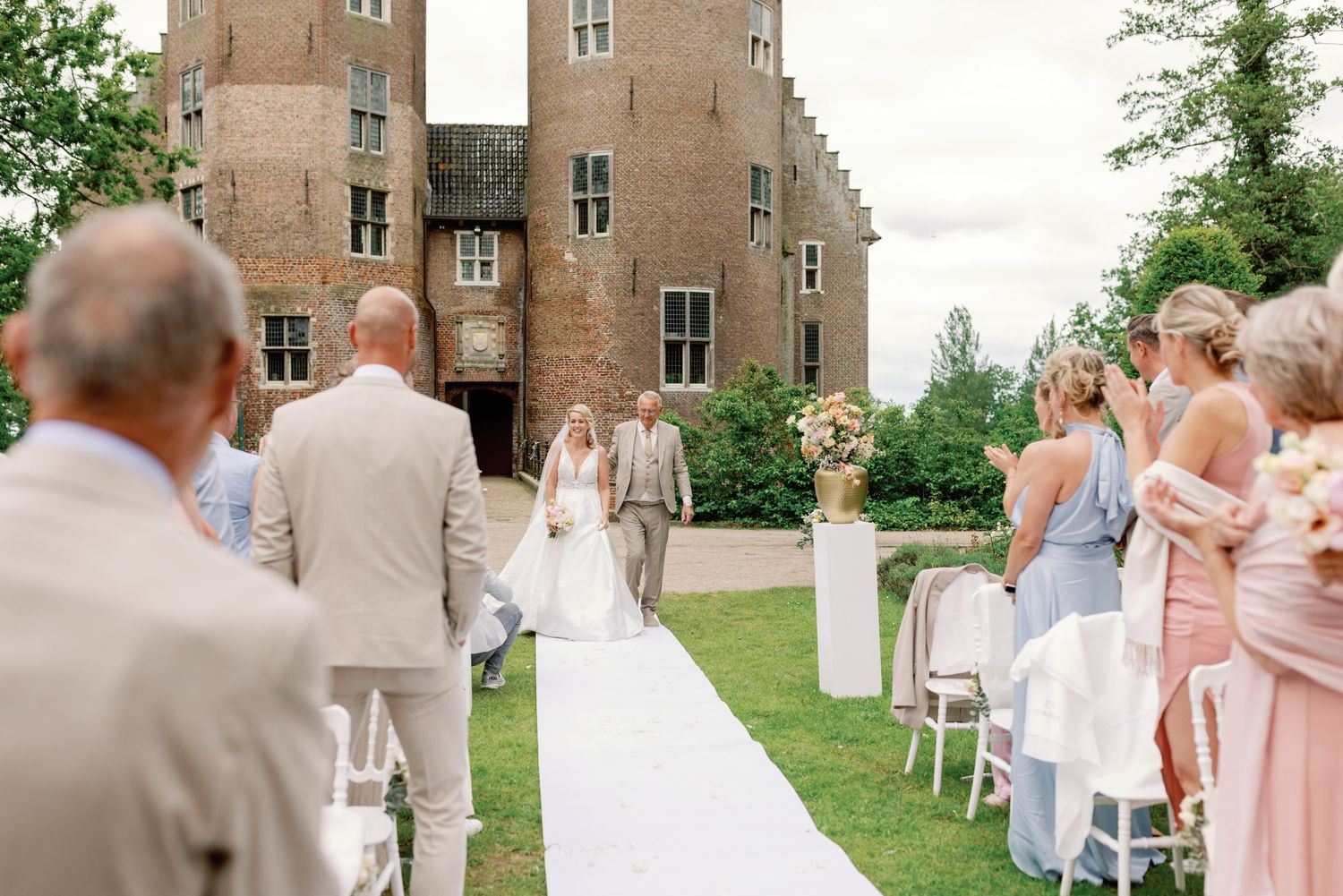 Outdoor wedding ceremony takes place on a lawn in front of a historic brick castle-like building.