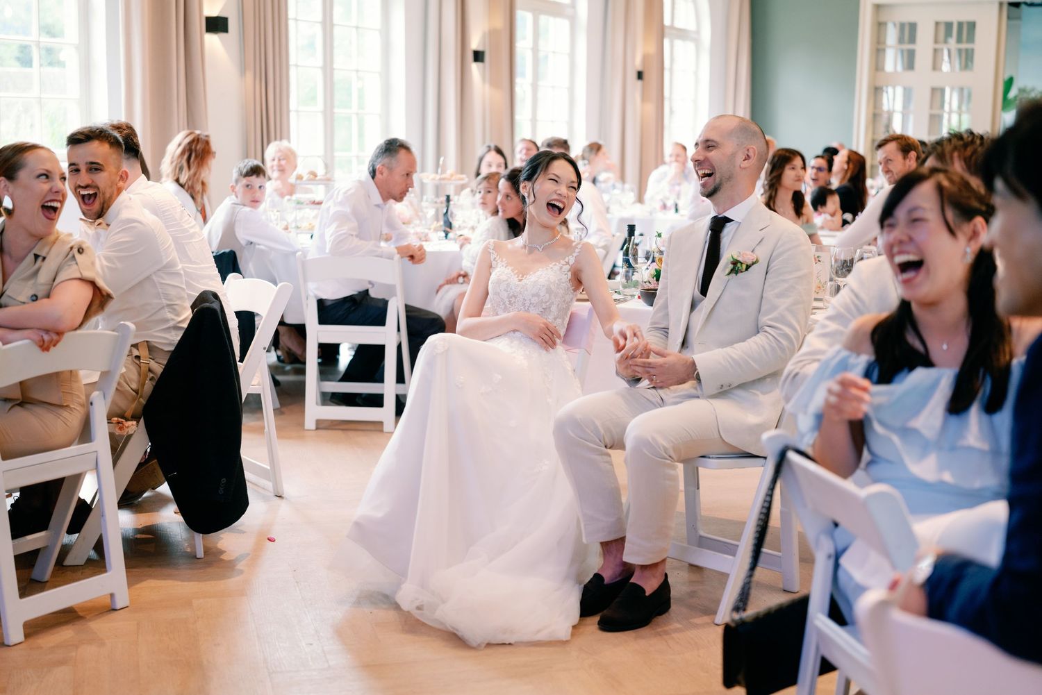 People dressed in all white outfits sit and laugh together during a social gathering in a bright indoor space.