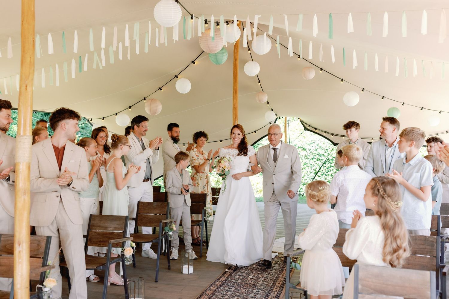 Wedding guests dance and celebrate at a reception under white string lights and lanterns in an elegant barn venue.