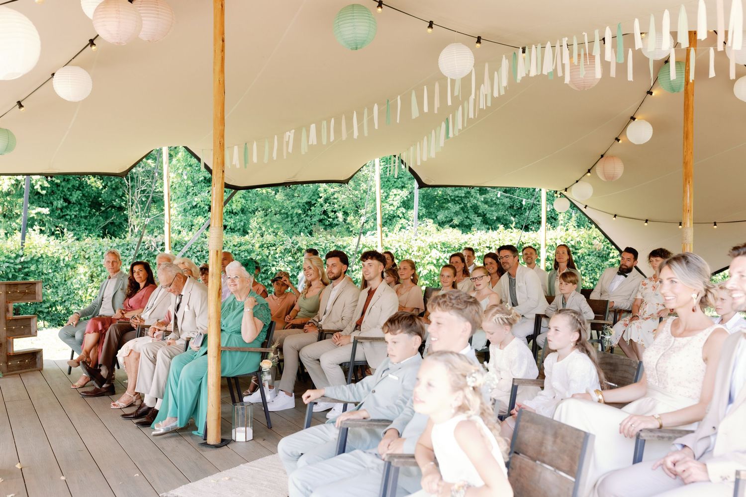 Wedding reception setup under white tent with string lights and round tables.