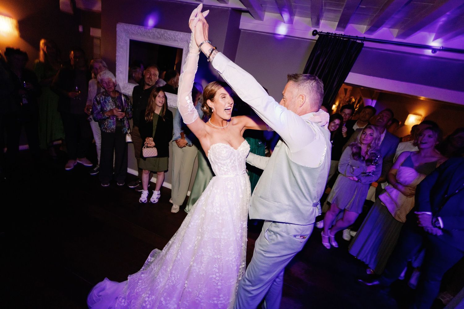 A couple dances together at a wedding reception with purple uplighting illuminating the dance floor.