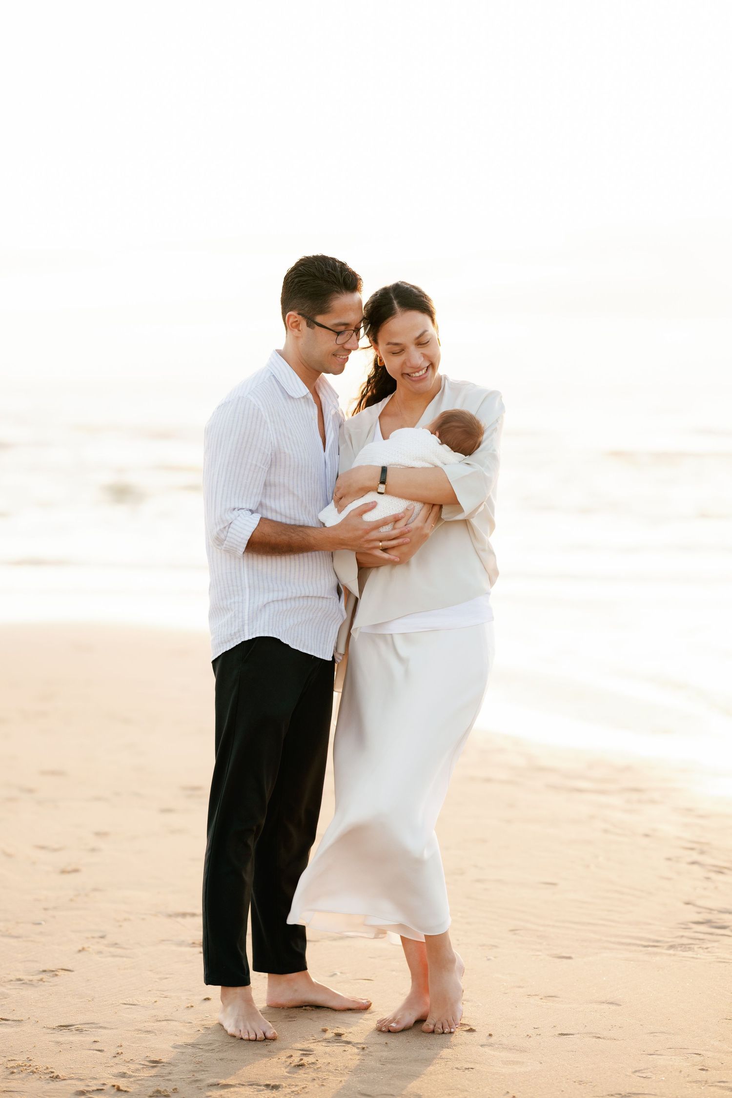 Family of three embraces on peaceful beach during golden hour.