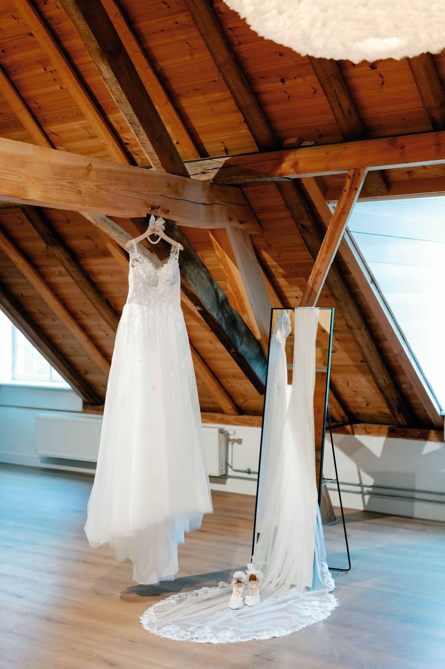 White wedding dresses displayed hanging from wooden beams in a rustic attic space with natural lighting.