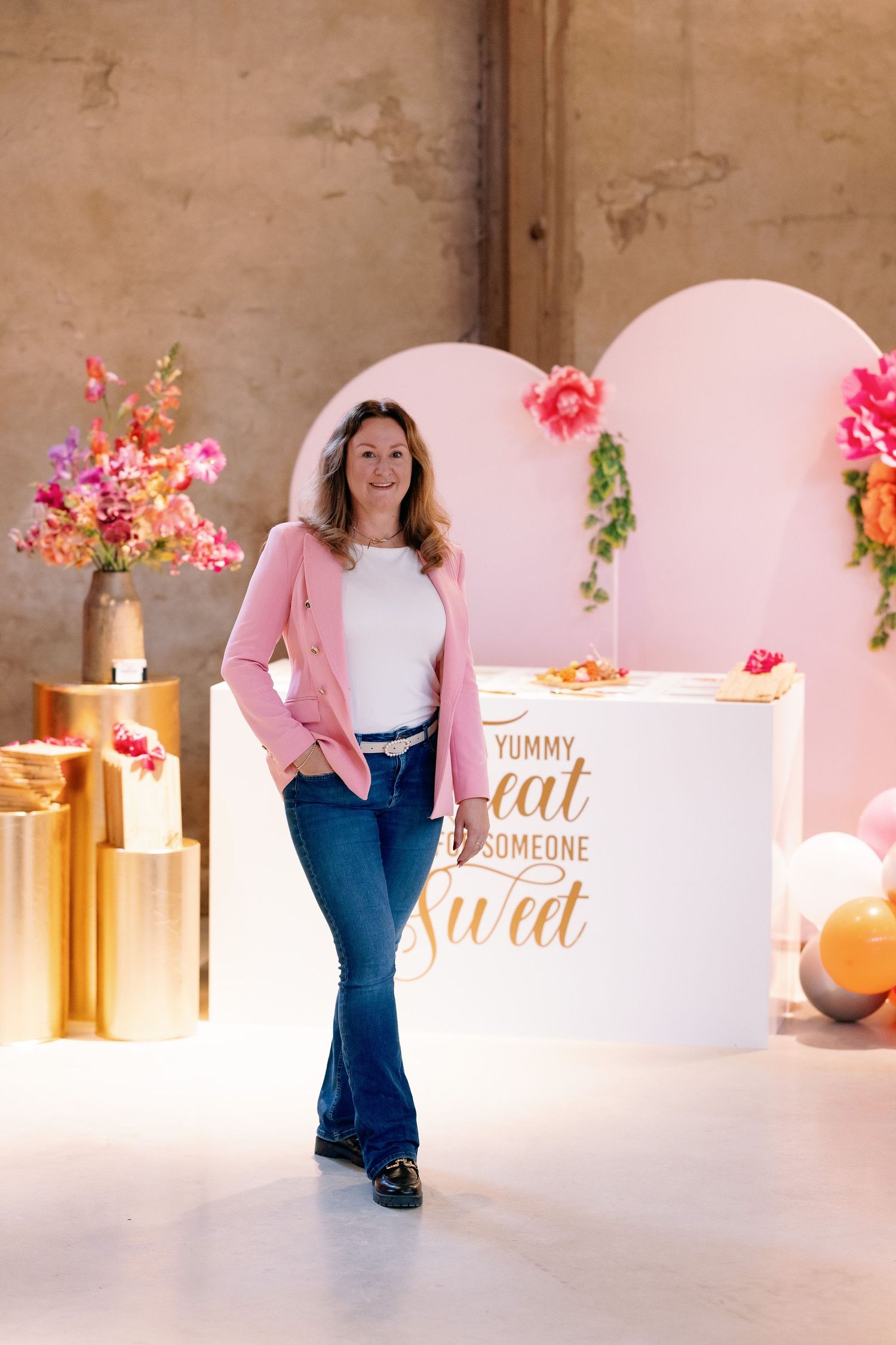 A photo series showing someone in a pink sweater and jeans posing against a pink backdrop with floral decorations.