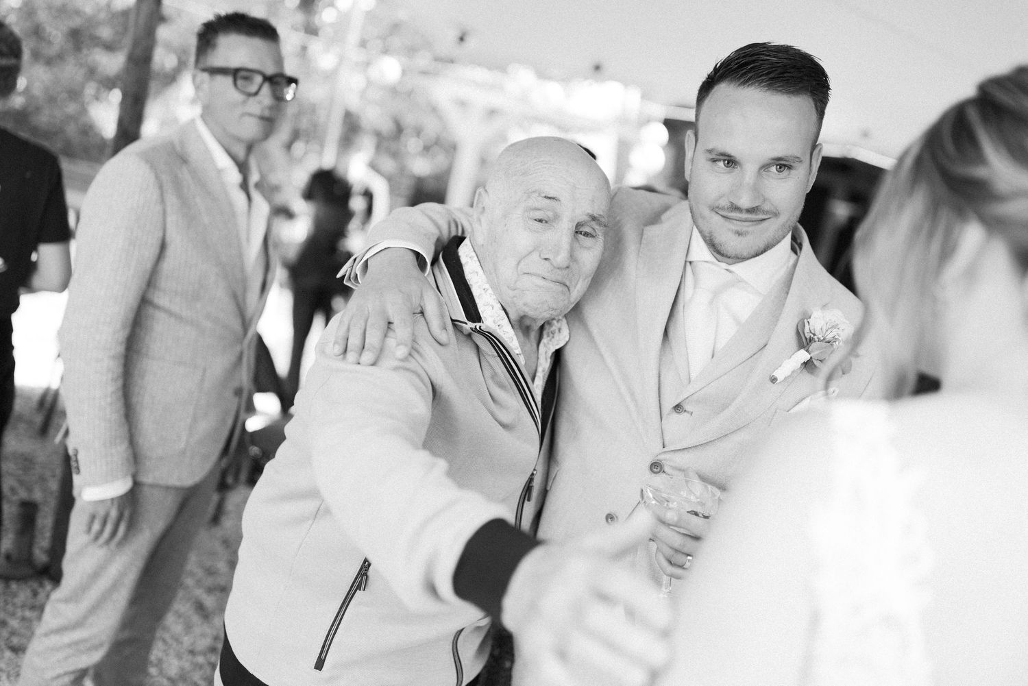 A black and white photo collage showing people at a wedding celebration with joyful expressions and formal attire.