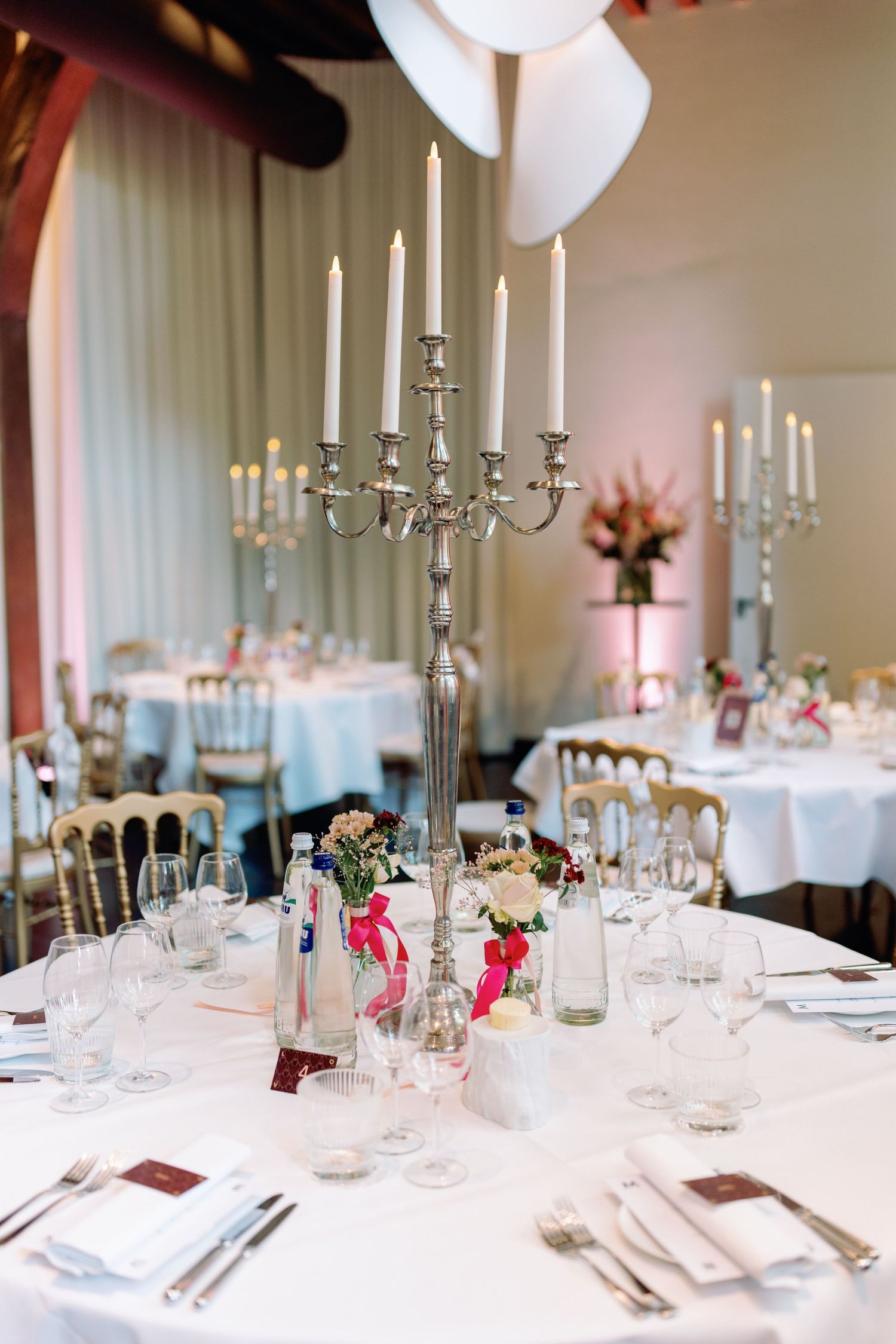 Elegant wedding reception table with tall silver candelabra centerpiece, white linens, and pink floral accents.