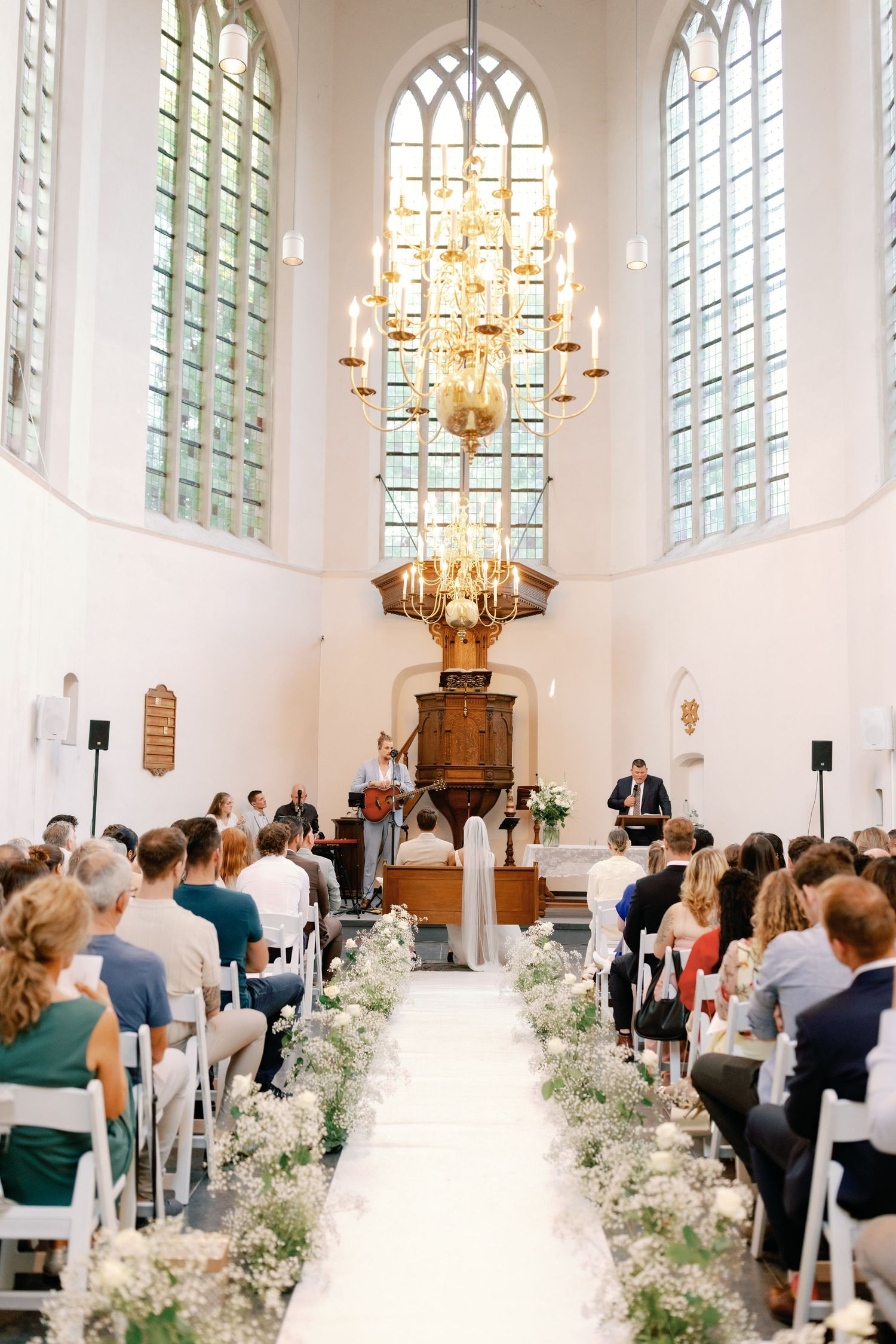Elegant church wedding ceremony with white aisle runner decorated with flowers and arched stained glass windows.