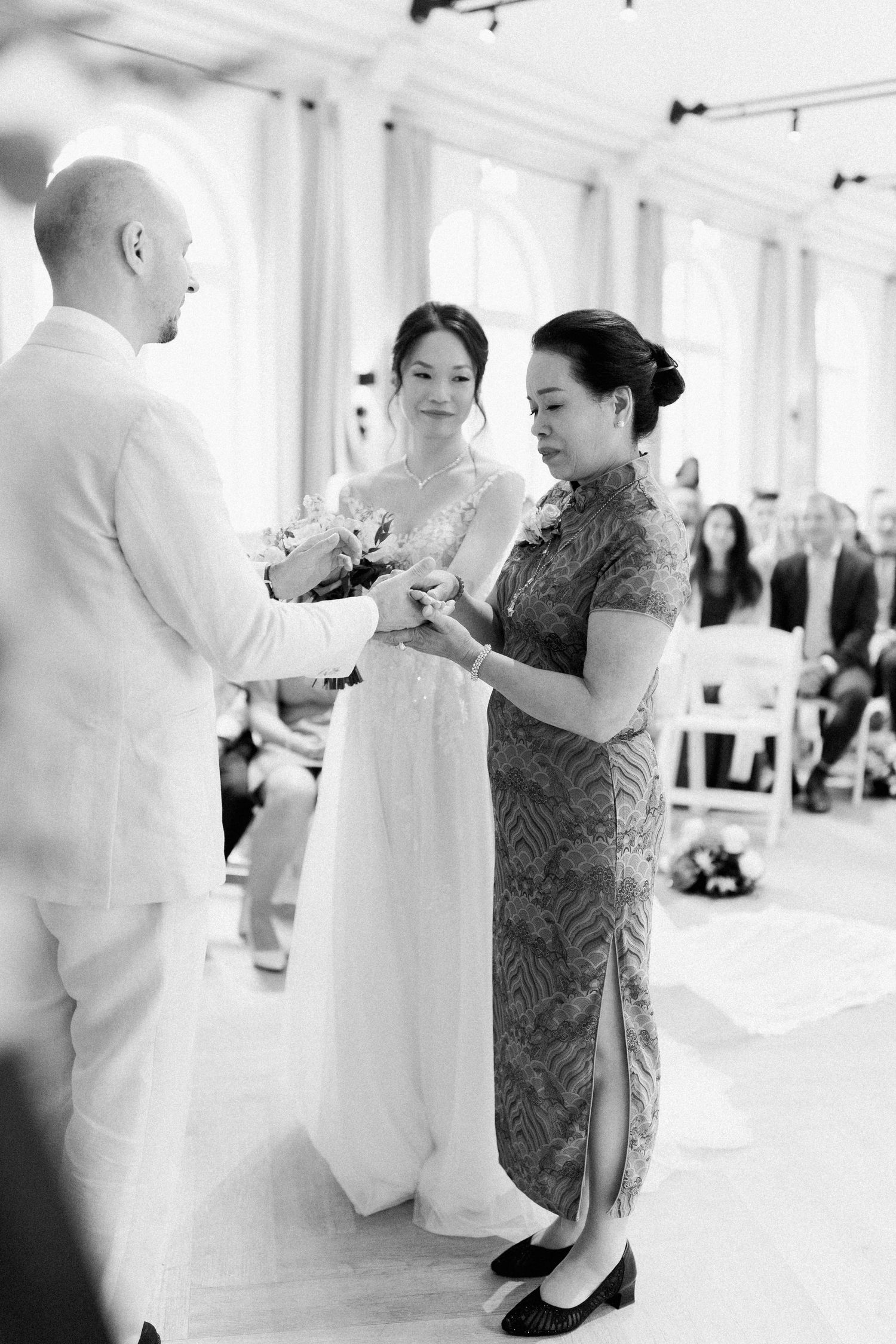 A tender moment during a wedding ceremony as a bride in white receives a blessing from an elder in a patterned dress.
