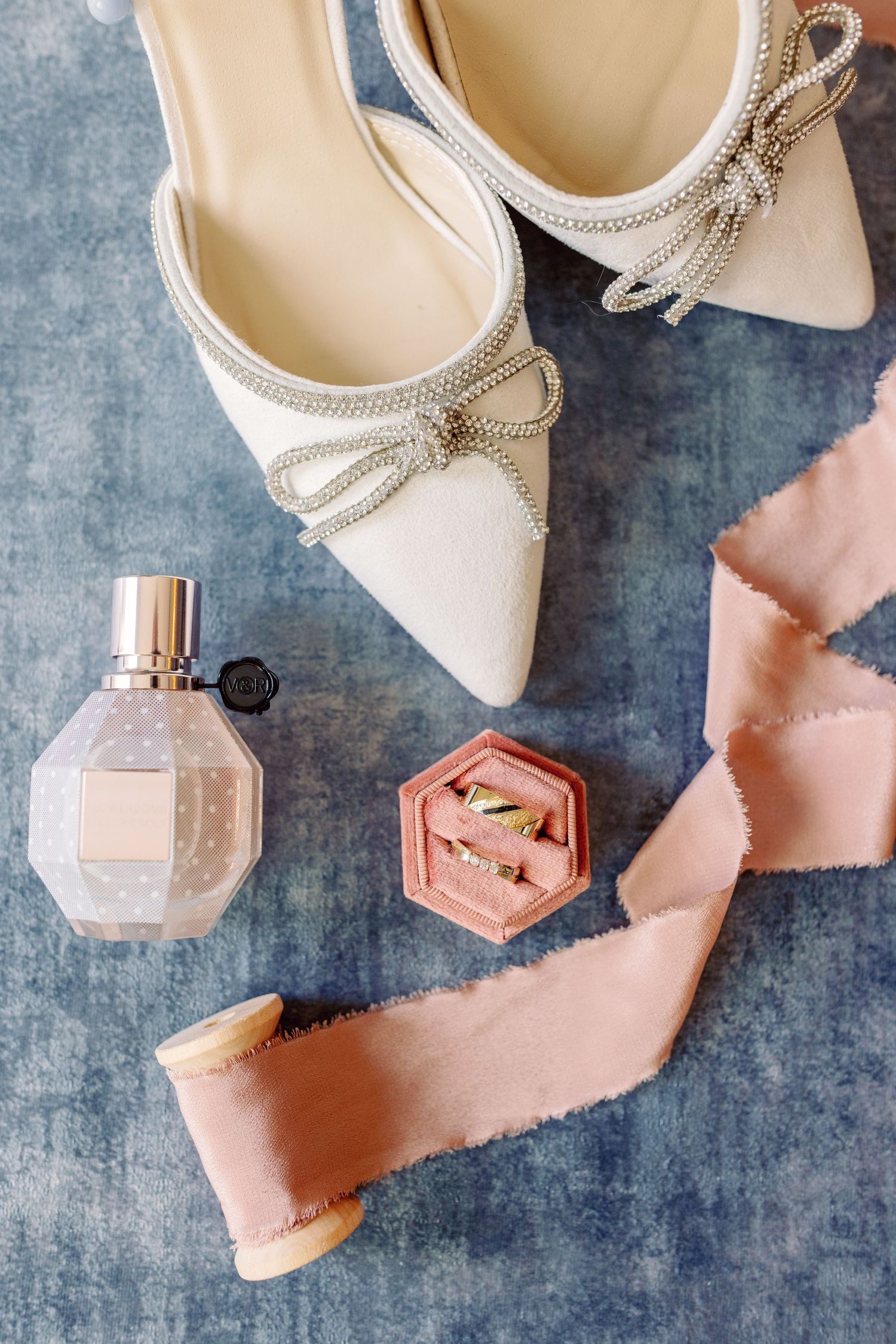 Elegant white bridal shoes with pearl details next to a pink perfume bottle on a gray surface.
