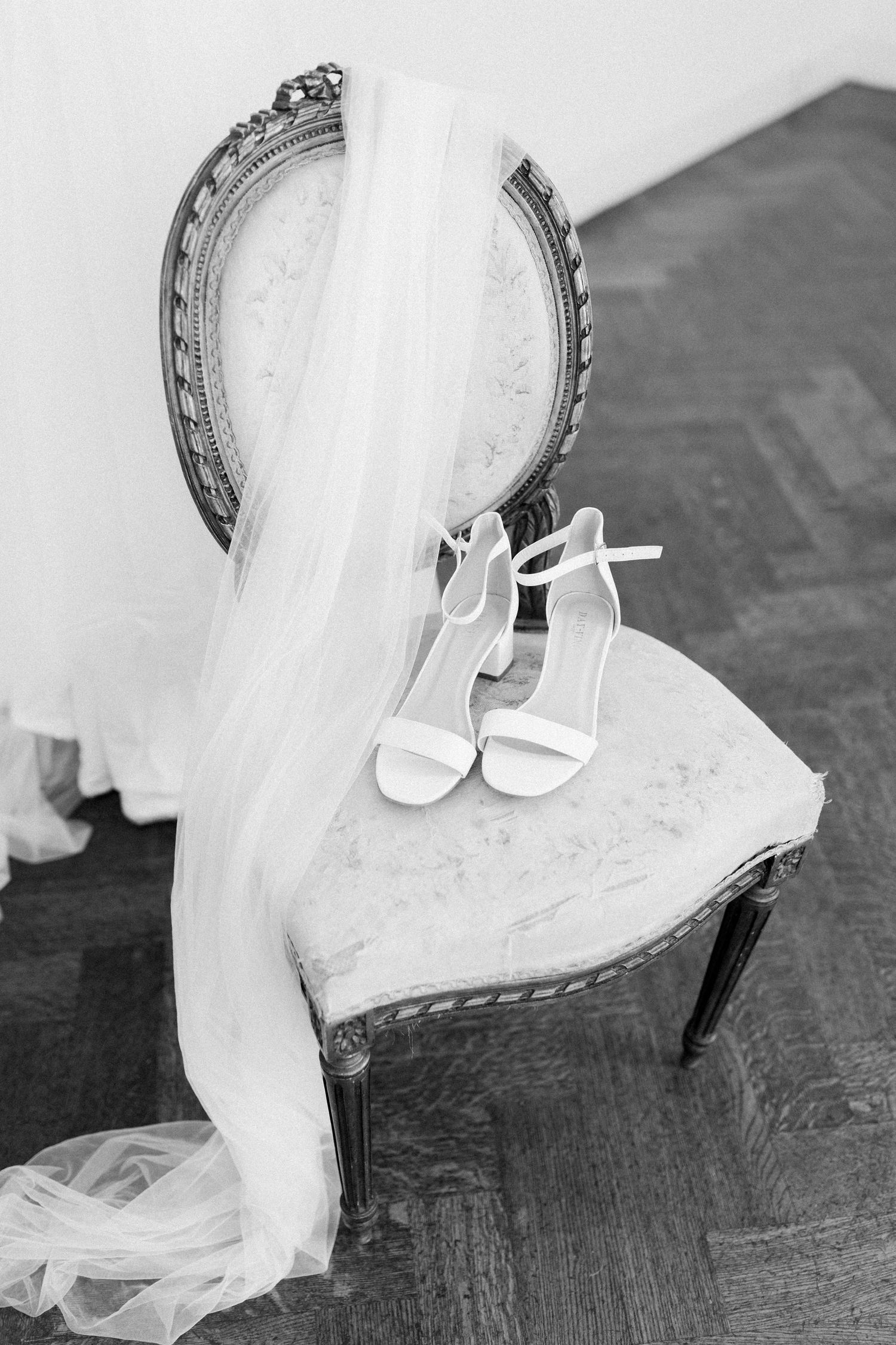 White bridal shoes rest elegantly on a wooden floor beside flowing wedding dress fabric.