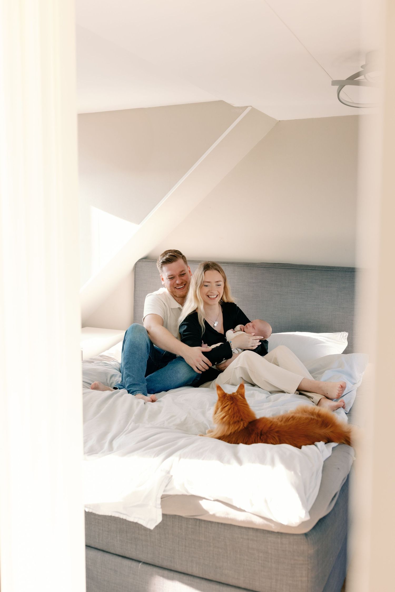 Family lounges on bed with orange cat in casual home setting.