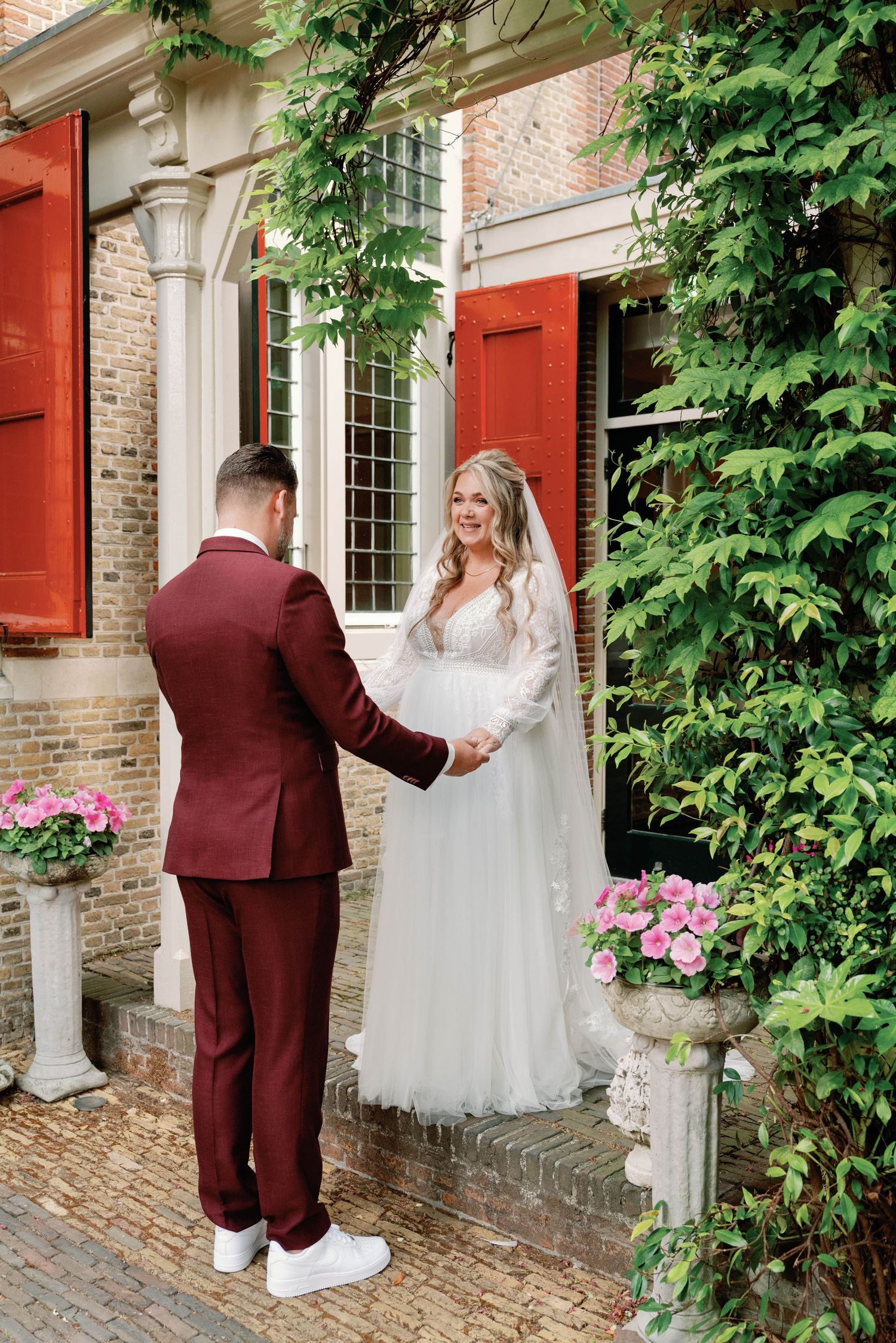 A romantic first look moment captured at a historic brick venue with climbing vines and burgundy shutters.