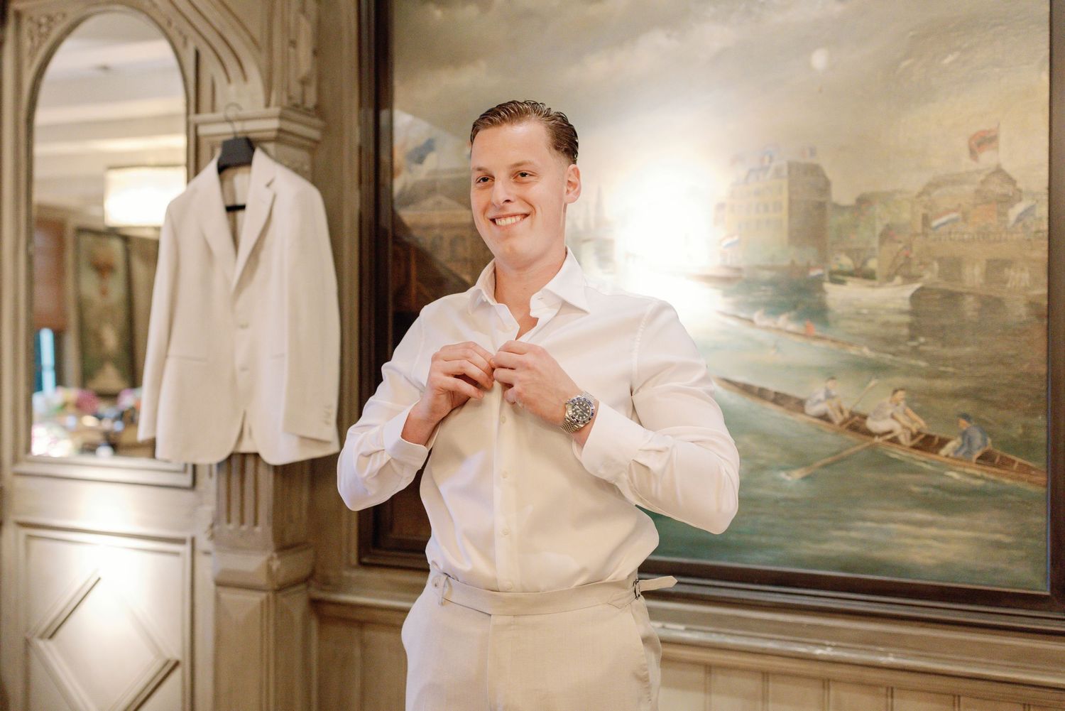 A group in light colored suits gather for formal photos in an elegant room with artwork and columns.