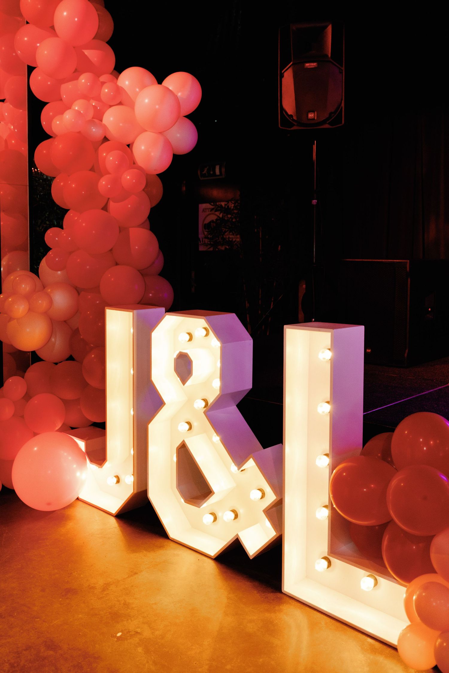 Large illuminated letters with pink balloon arch decorations create a romantic event display against a dark background.