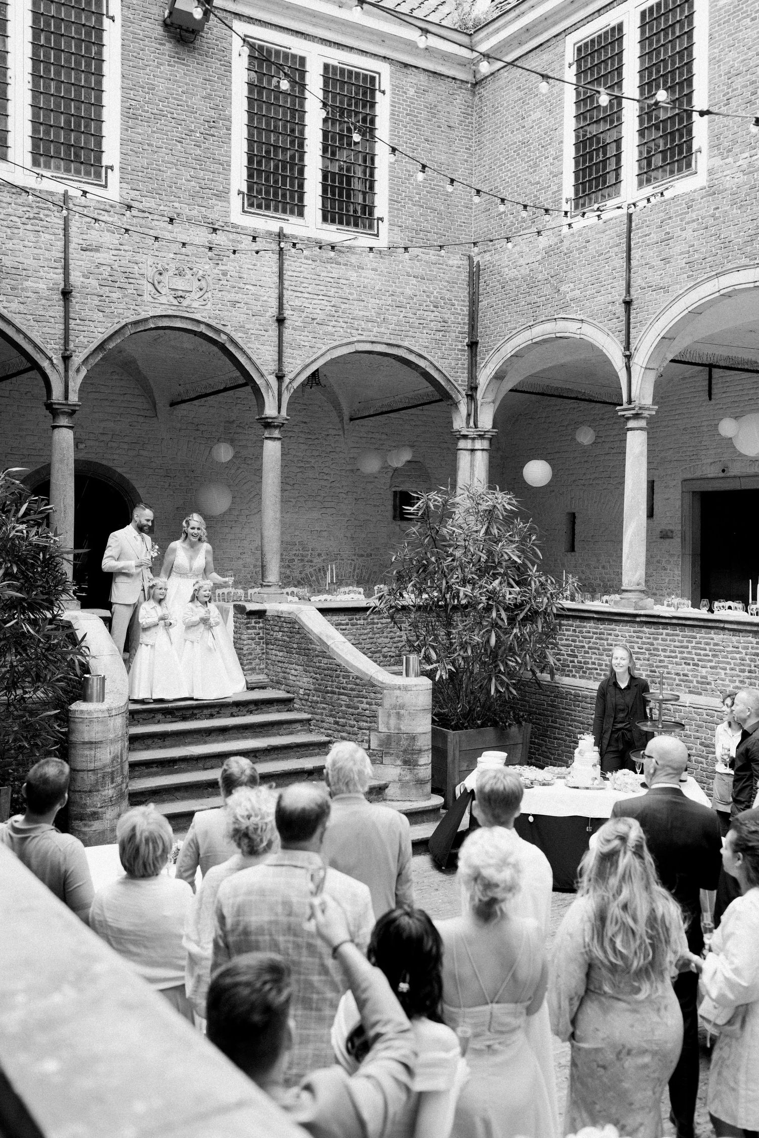 Black and white photo of a wedding ceremony in a historic courtyard with arched columns and brick walls.
