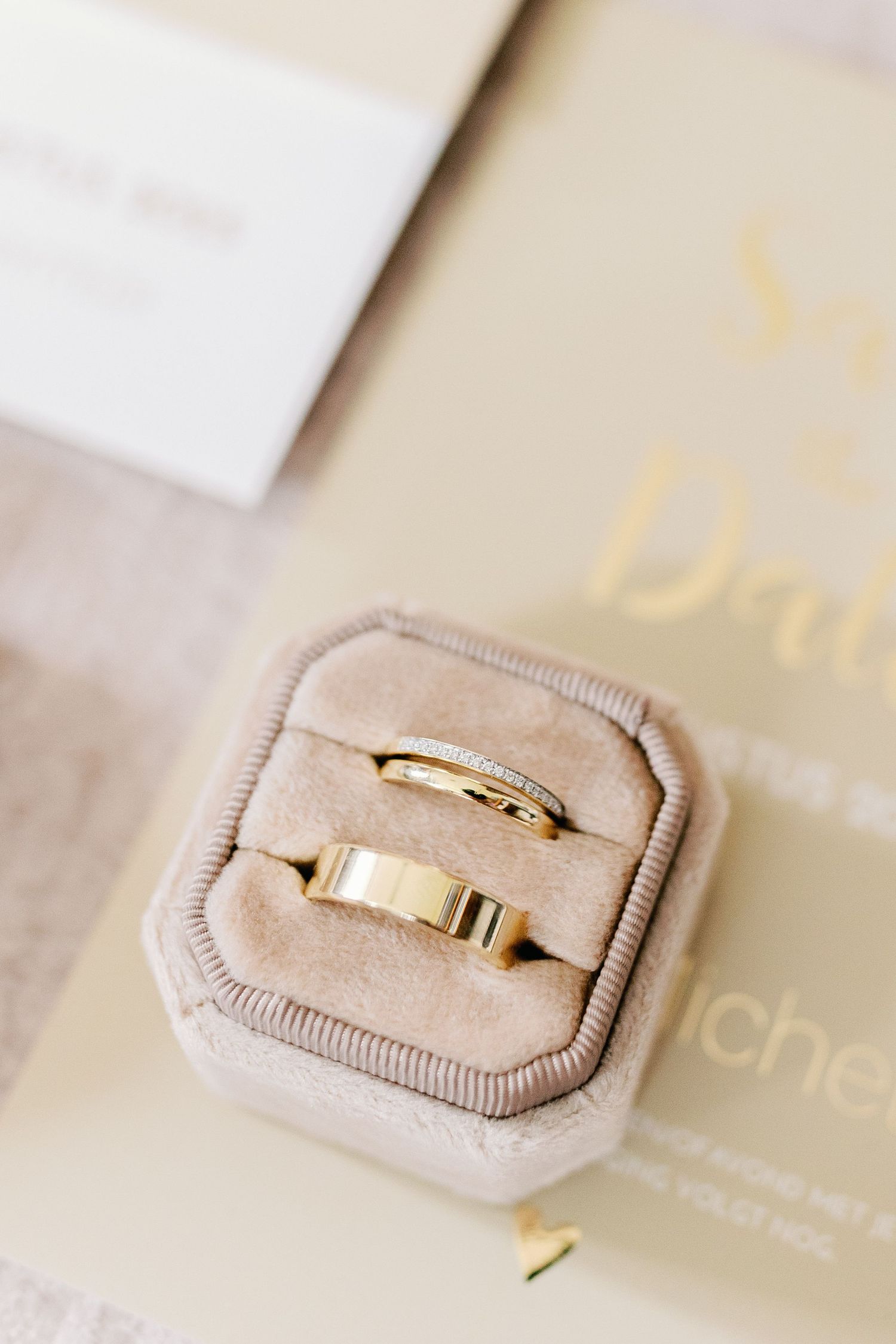 Gold wedding band with delicate bow design rests elegantly in a beige velvet ring box.