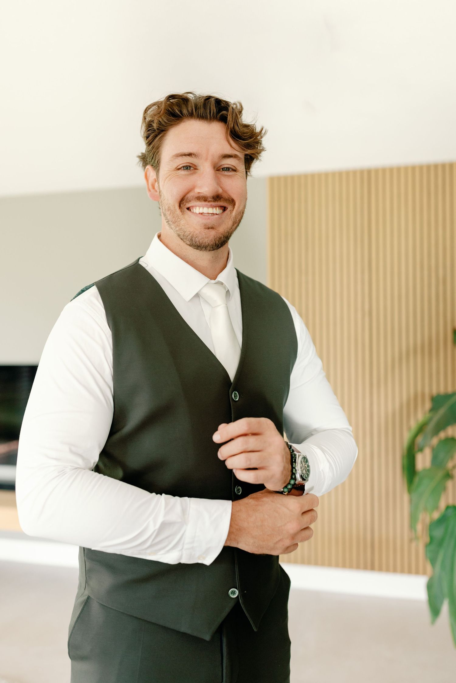 Professional wearing a dark vest and white dress shirt stands in a bright modern interior with minimal decor.